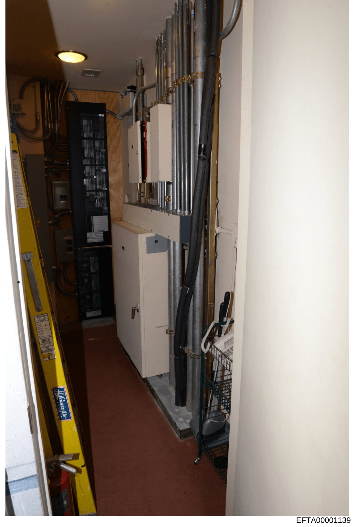 This is an evidence photograph showing an interior electrical/mechanical room containing a main electrical panel, conduit systems, and related building infrastructure. The image documents the physical layout of critical building systems, likely taken