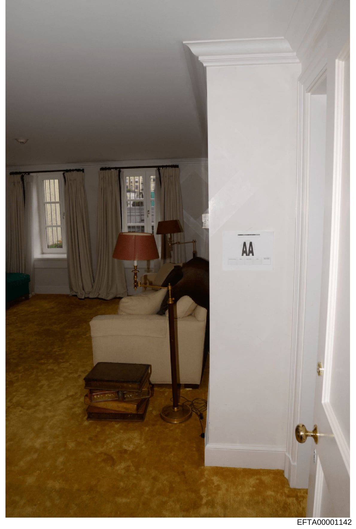 This is an evidence photograph from the Epstein investigation showing an interior room with formal furnishings. The image depicts a living or sitting area with cream-colored upholstered furniture, red-shaded lamps, wooden side tables, curtained windo