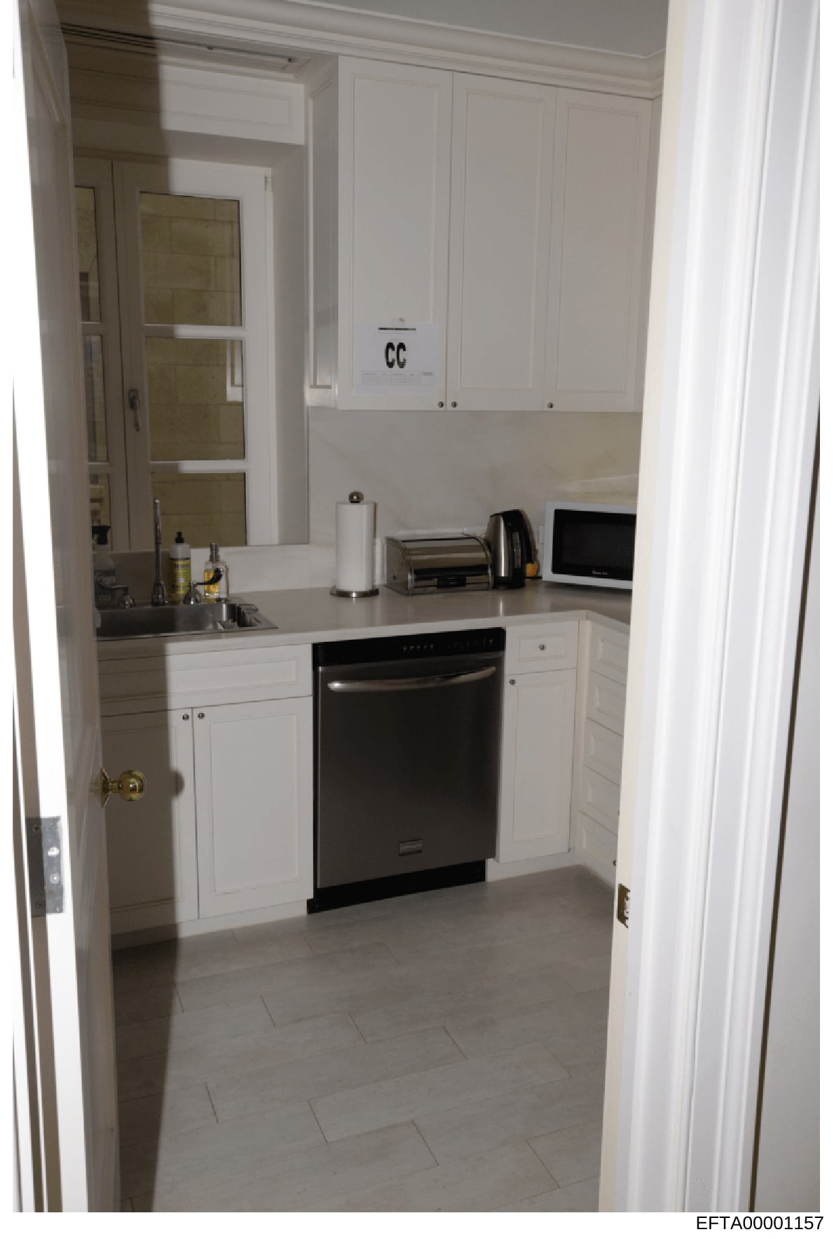 This is a photograph of a modern kitchen interior featuring white cabinetry, stainless steel appliances, and light tile flooring. The image includes an evidence marking 'CC' visible on the upper cabinet, indicating this is a crime scene or investigat