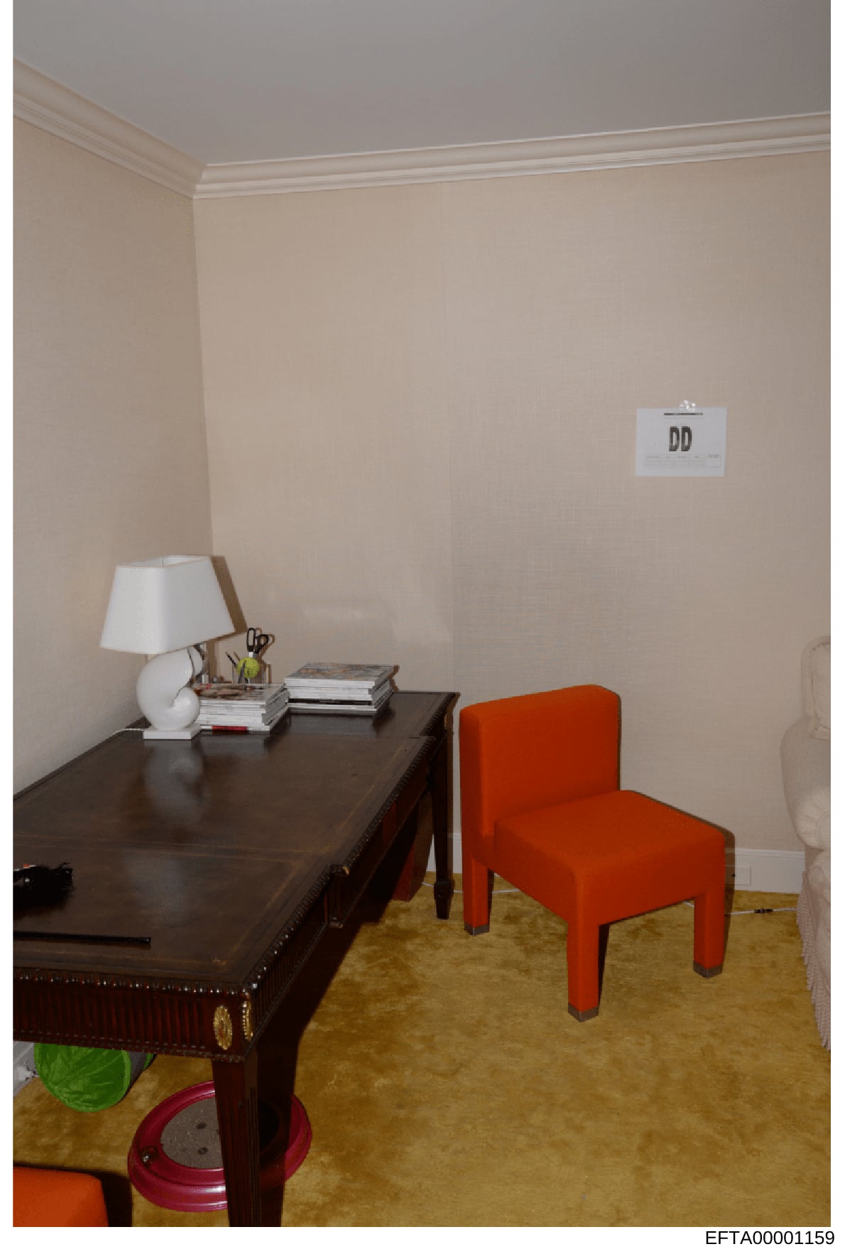 This is an evidence photograph showing an interior room space with furnishings, marked with evidence label 'DD'. The room features a dark wooden desk with a white table lamp, stacked books, and writing implements, paired with a bright orange upholste