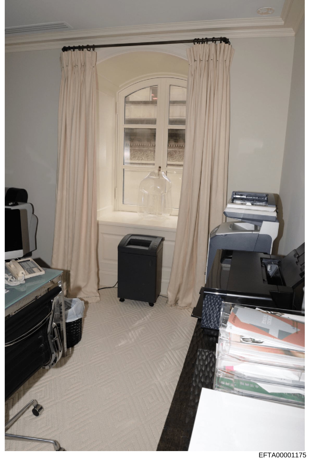 This is an evidence photograph showing an interior room with professional office equipment, including a dehumidifier, printer, stacked documents/magazines, and a computer monitor. The room features cream-colored curtains framing an arched doorway wit