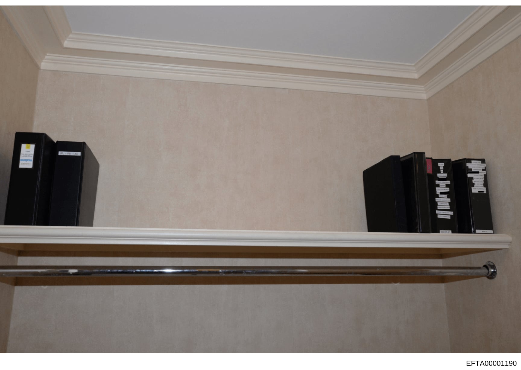 This is an evidence photograph showing a wall-mounted shelving unit containing multiple black binders and file boxes, each labeled with evidence tags or identification markers. The photo appears to be documentation of seized materials or physical evi