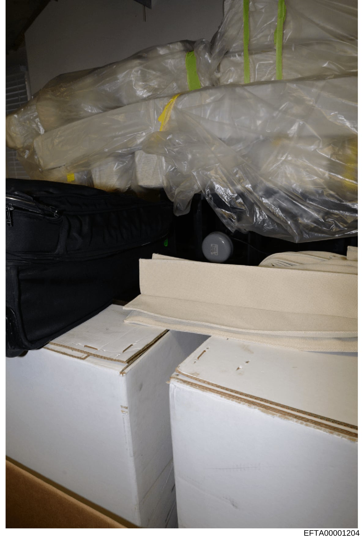 This is an evidence photograph showing multiple sealed plastic-wrapped packages with yellow and green evidence tape markers, stacked alongside white cardboard boxes. The image appears to be from a property seizure or evidence collection operation, wi
