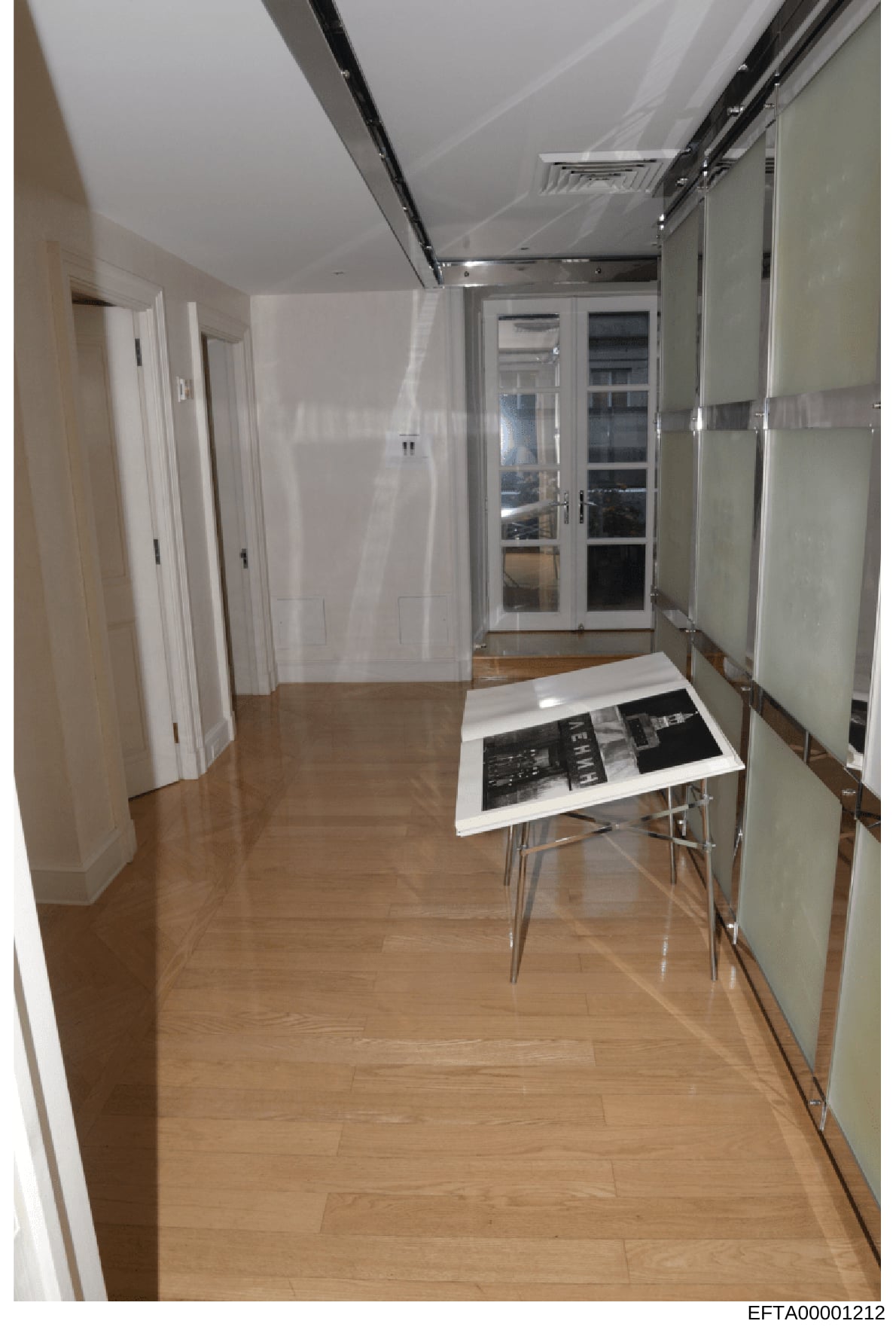 This is an evidence photograph showing a modern hallway interior with white walls, wood flooring, and contemporary design features. The image appears to be part of property documentation during the investigation, showing the layout and condition of i