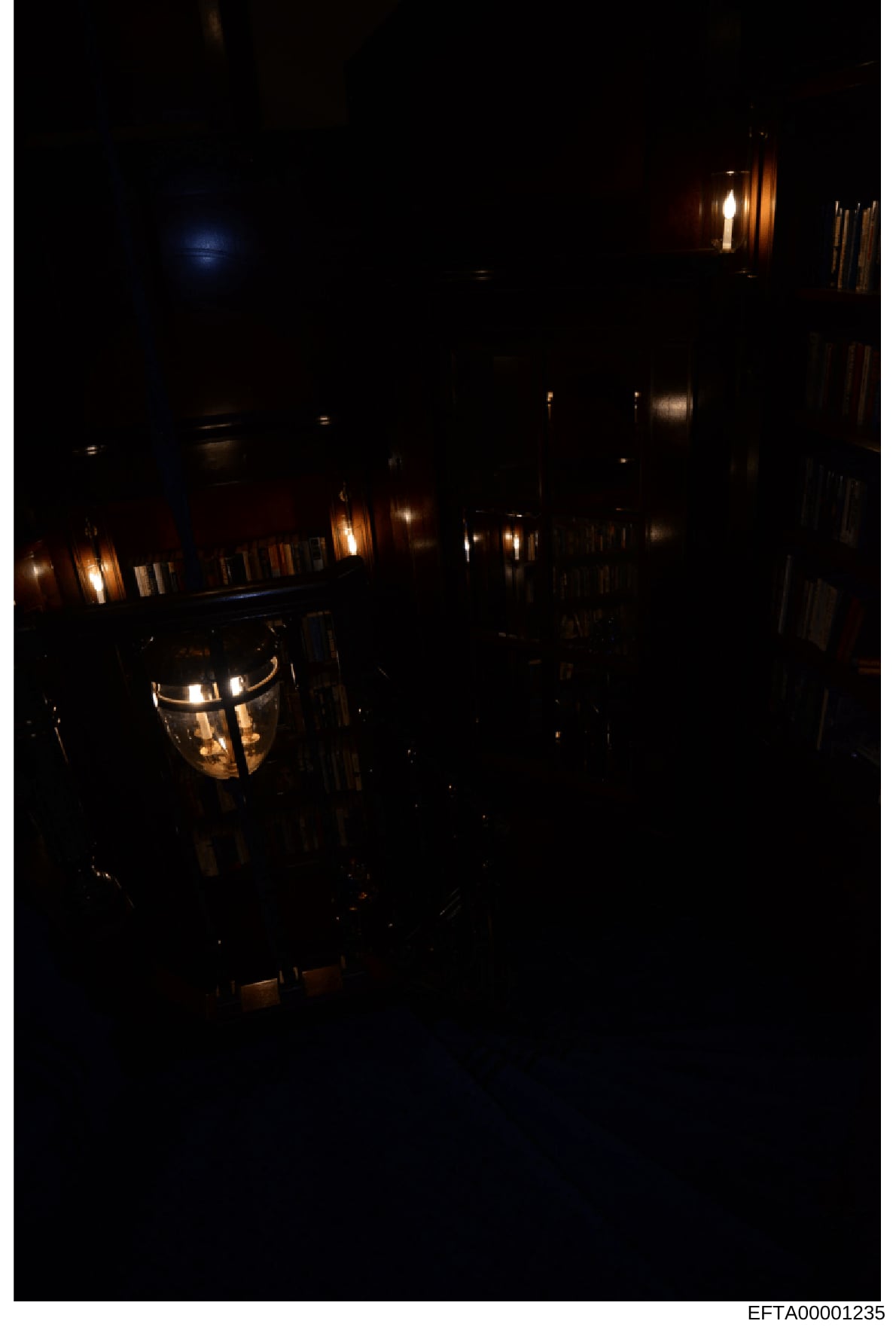 This is a nighttime photograph of an interior space, likely a hallway or corridor in a residential or commercial property. The image shows multiple wall-mounted light fixtures (sconces) illuminating the space with warm, golden lighting against dark w