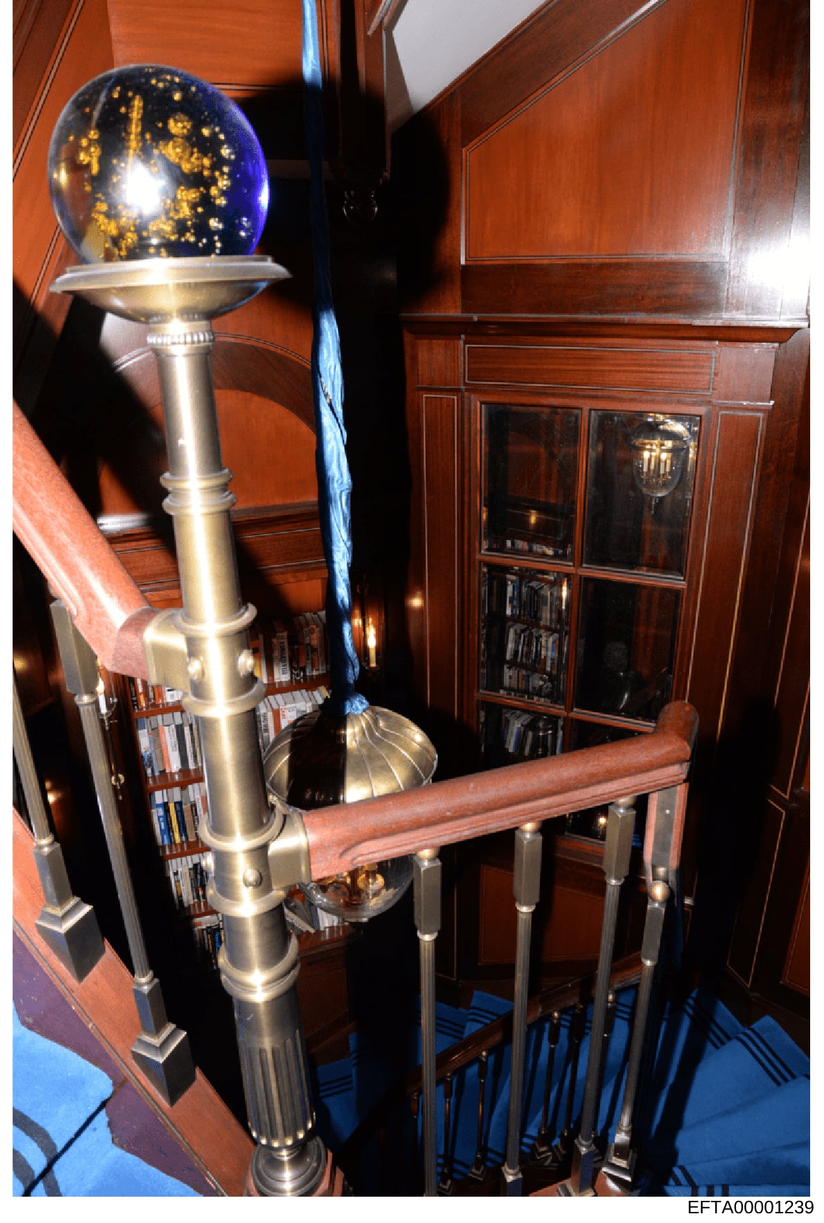This photograph documents the interior of an upscale residential space, showing a brass floor lamp with a blue and gold decorative globe, wooden cabinetry with glass display cases, and rich wood paneling. The image appears to be evidence documentatio