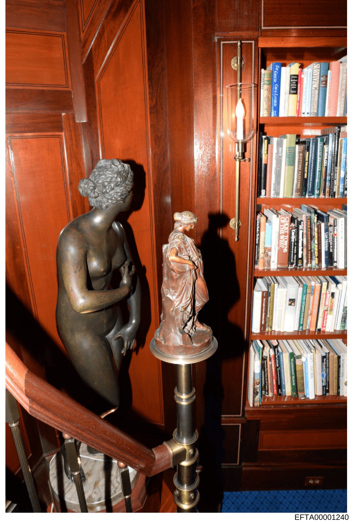 This is a photograph of an interior room featuring decorative bronze sculptures, mahogany wood paneling, built-in bookshelves with books, and period furnishings. The image appears to be documentation of a property's interior, possibly from one of Jef