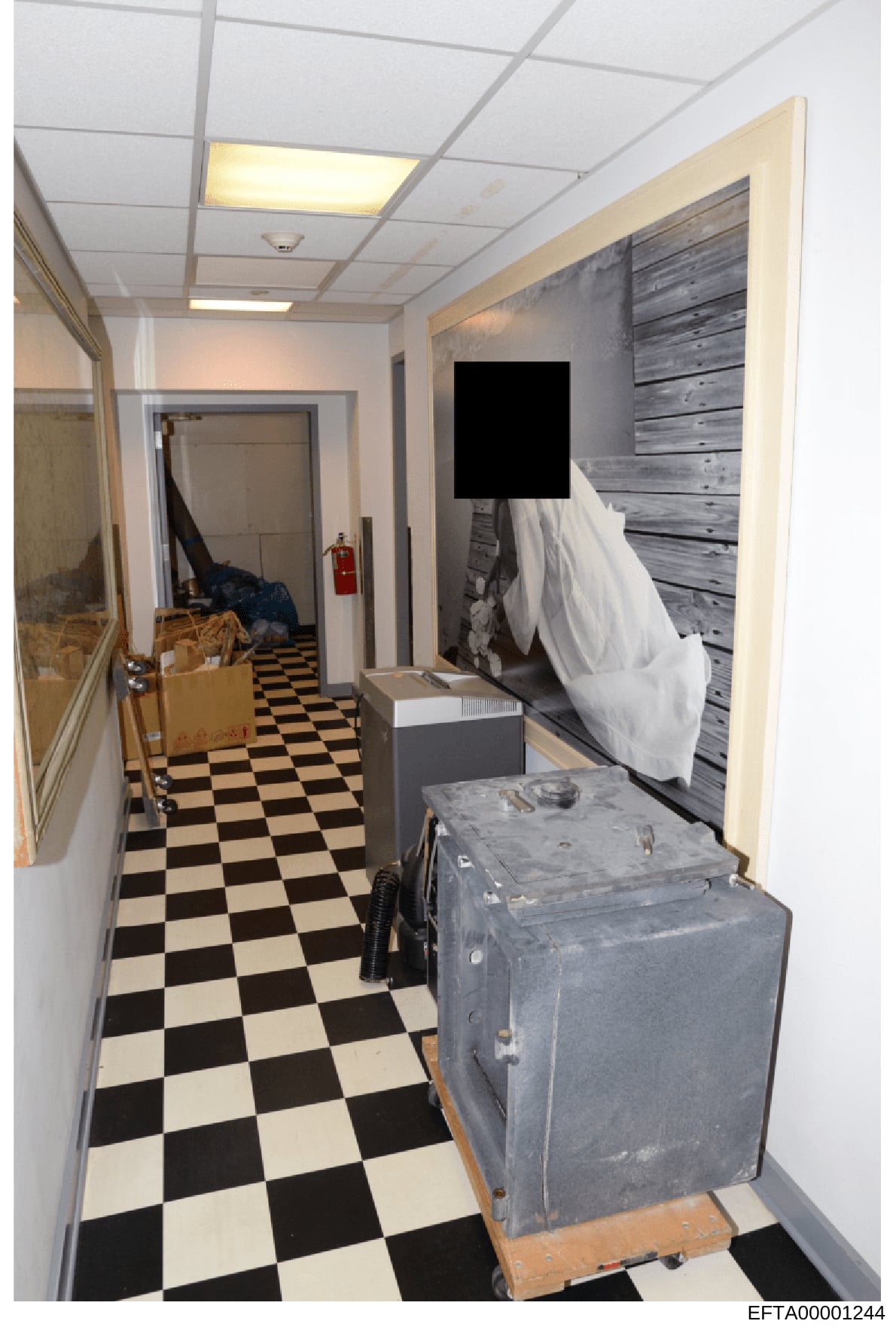 This is a photograph of an interior basement or utility hallway showing storage items, equipment, and general conditions. The image depicts a space with distinctive black and white checkered flooring, drop ceiling with recessed lighting, and various