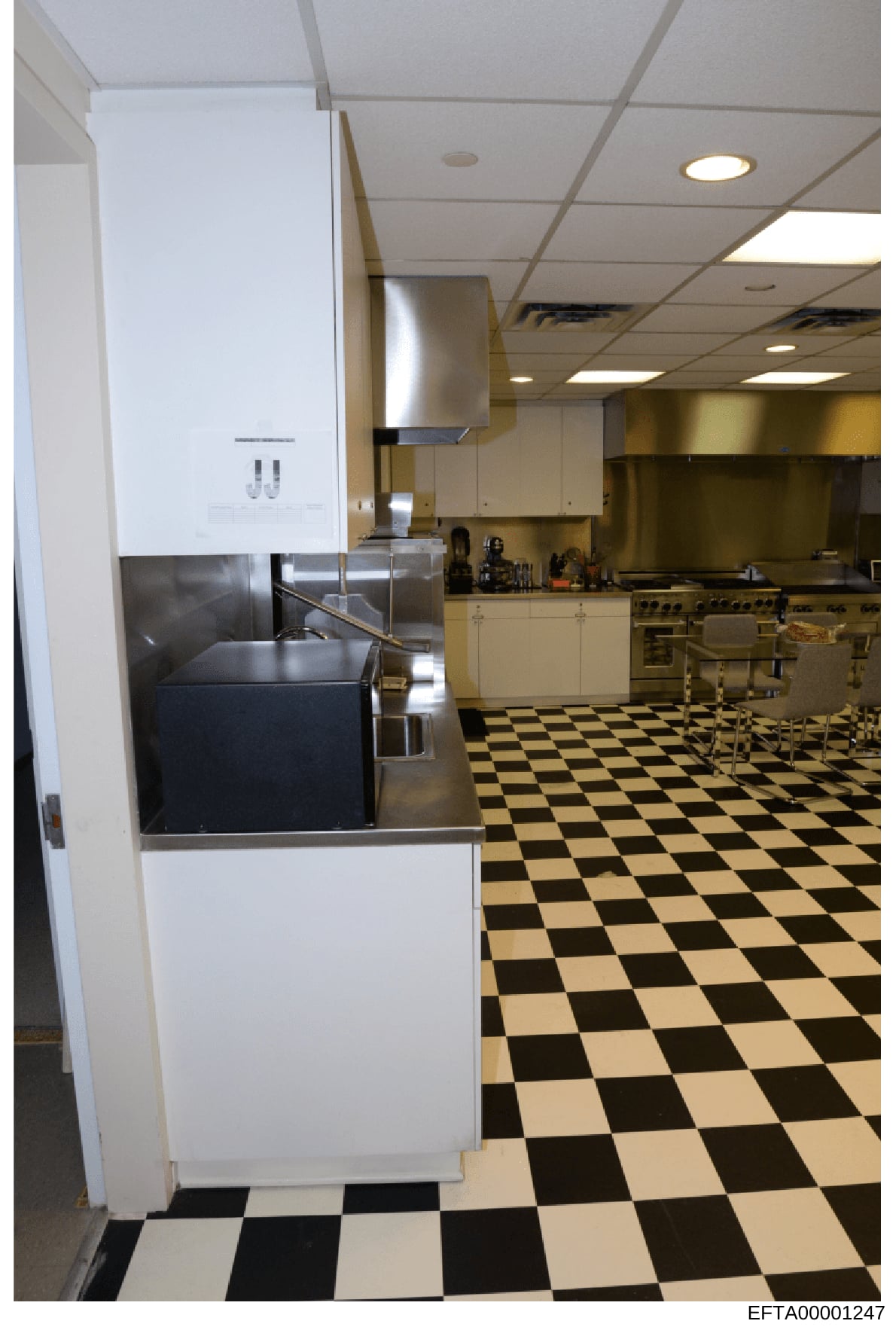 This is an evidence photograph of a large commercial-style kitchen interior, likely from one of Jeffrey Epstein's properties. The photo shows a spacious kitchen with professional-grade stainless steel appliances, white cabinetry, and distinctive blac