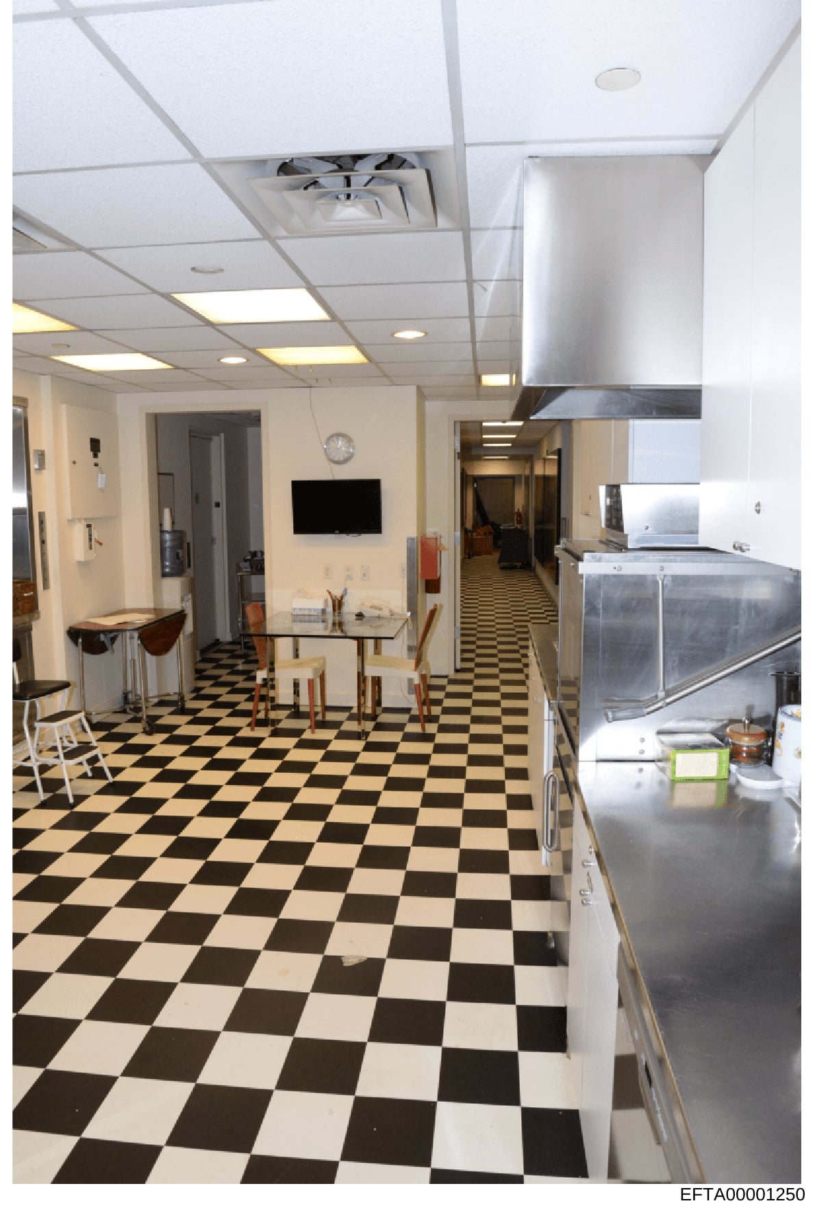 This is an evidence photograph documenting the interior of a kitchen and common area space, featuring a distinctive black and white checkered floor pattern, stainless steel appliances, drop ceiling with recessed lighting, and a mounted television. Th