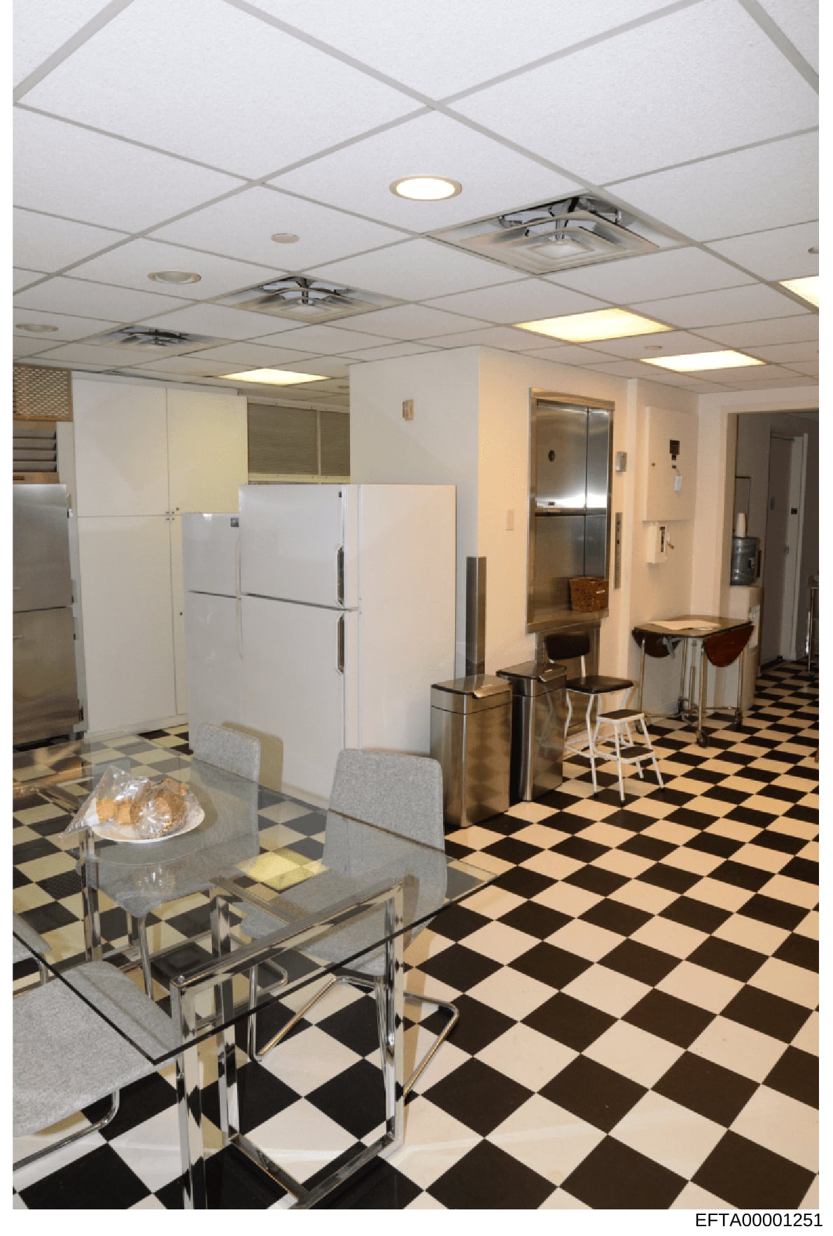 This photograph depicts a commercial or institutional kitchen interior, featuring multiple refrigerators, a checkerboard tile floor, fluorescent ceiling panels, and bar seating. The image appears to be documentation of an Epstein-related property's i