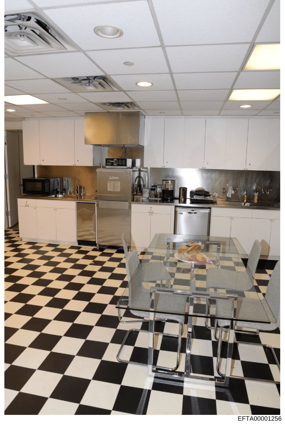 This photograph documents the interior kitchen of an Epstein property, showing a modern kitchen with white cabinetry, stainless steel appliances, a metal dining table with chairs, and a distinctive black-and-white checkered floor. The image appears t