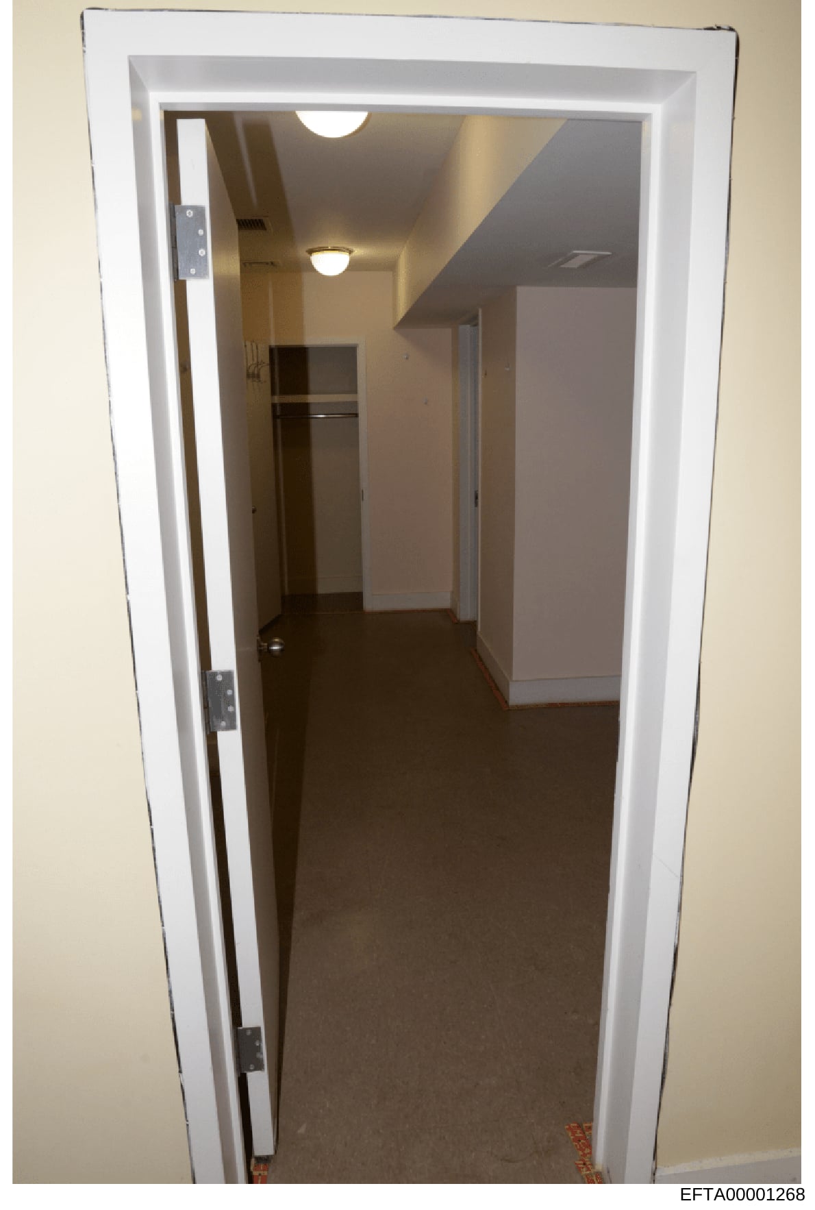 This is a photograph of an interior hallway or corridor, likely taken as part of property documentation or evidence collection during the investigation. The image shows a narrow passage with white-trimmed doorways, fluorescent ceiling lighting, dark