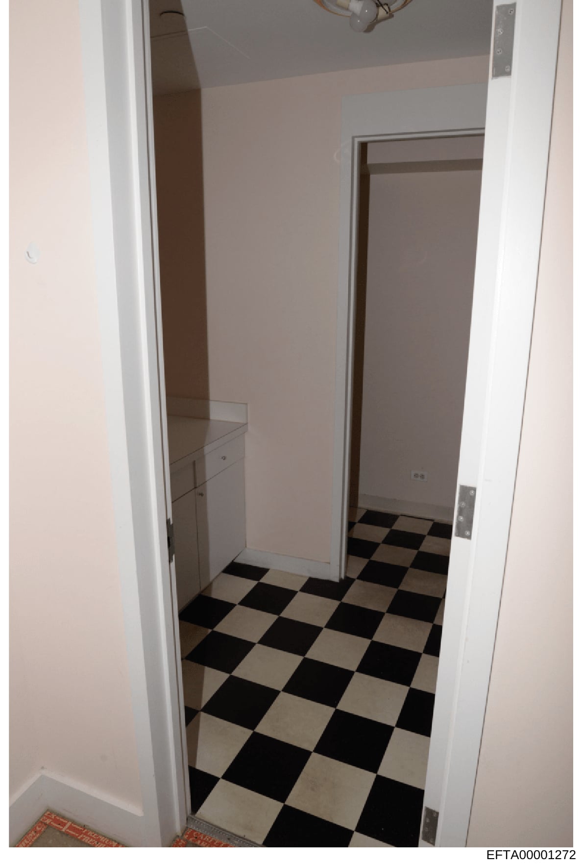 This is an evidence photograph showing the interior of what appears to be a bathroom or utility room, featuring a black and white checkered tile floor, white walls, and built-in fixtures. The photo was taken as part of the Epstein investigation docum