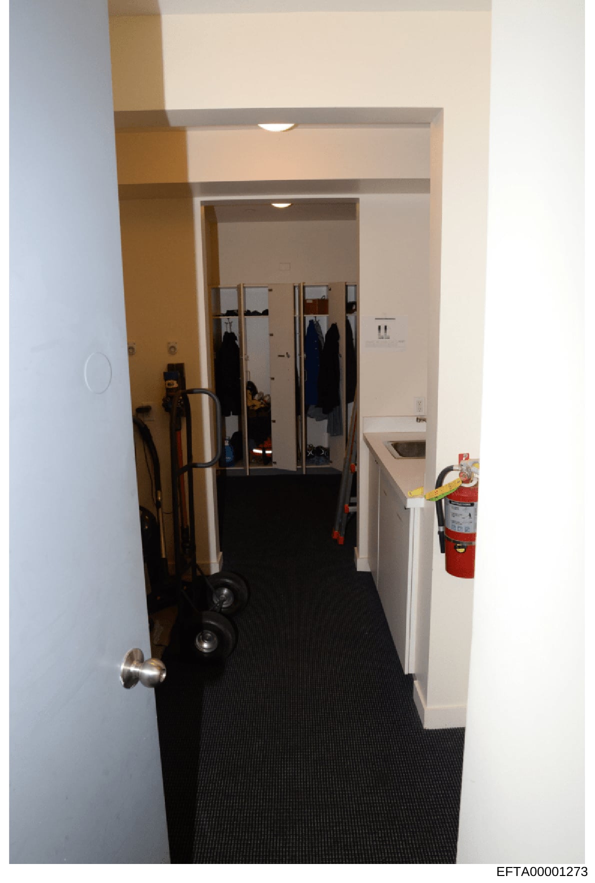 This photograph shows an interior hallway or corridor of an office or commercial building, featuring a mirrored closet with sliding doors, storage shelves with dark clothing, a fire extinguisher mounted on the wall, and various items including a hand