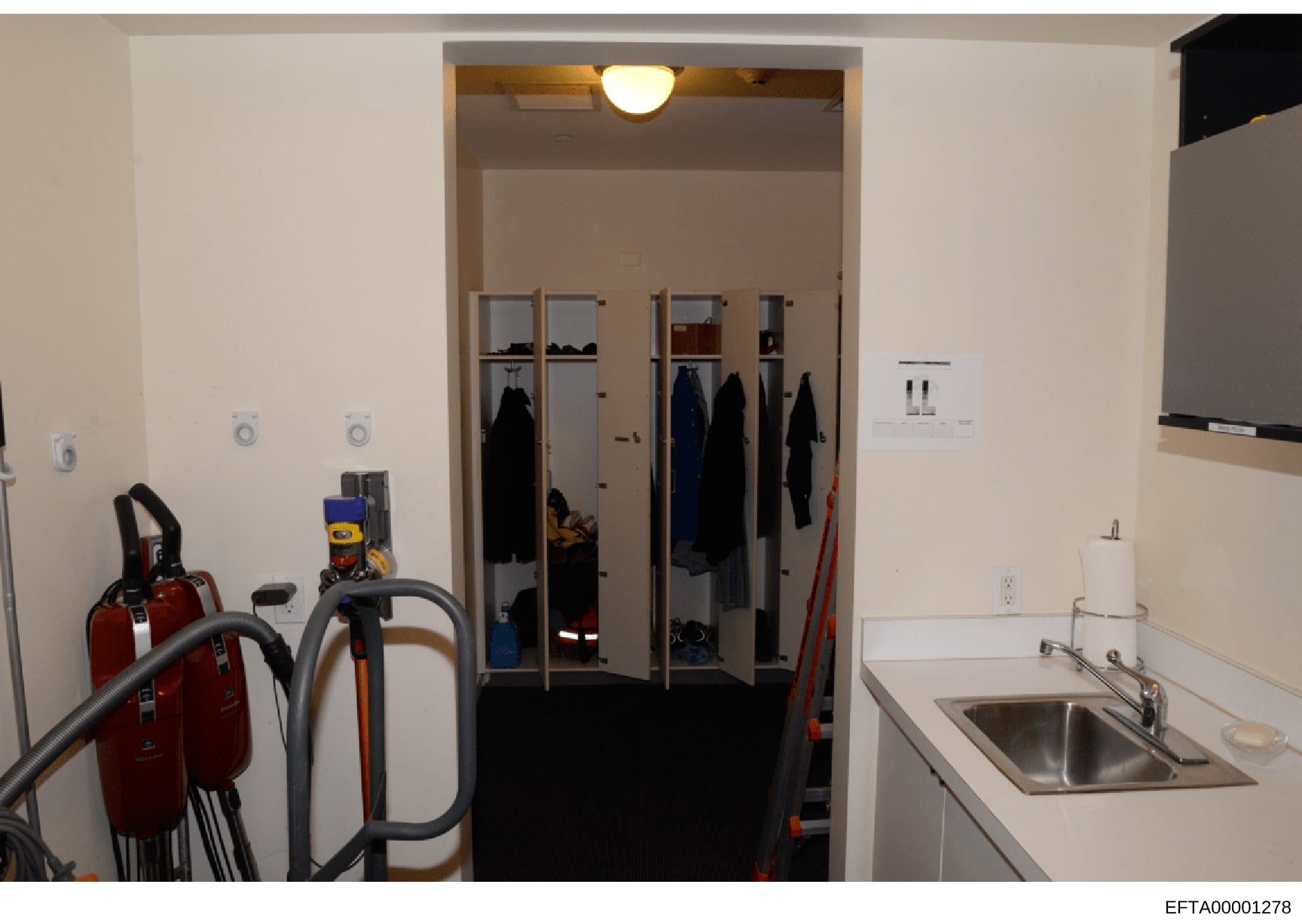 This is an evidence photograph showing the interior of a utility or service room, featuring a large closet with glass doors containing hanging clothing and personal items, cleaning equipment stored on the left side, and a sink on the right. The photo