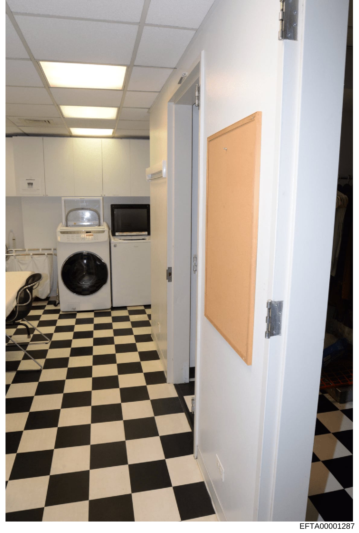 This photograph documents an interior laundry facility featuring standard household appliances including a washing machine, dryer, and television mounted on the wall. The room has distinctive black and white checkerboard flooring, recessed ceiling li
