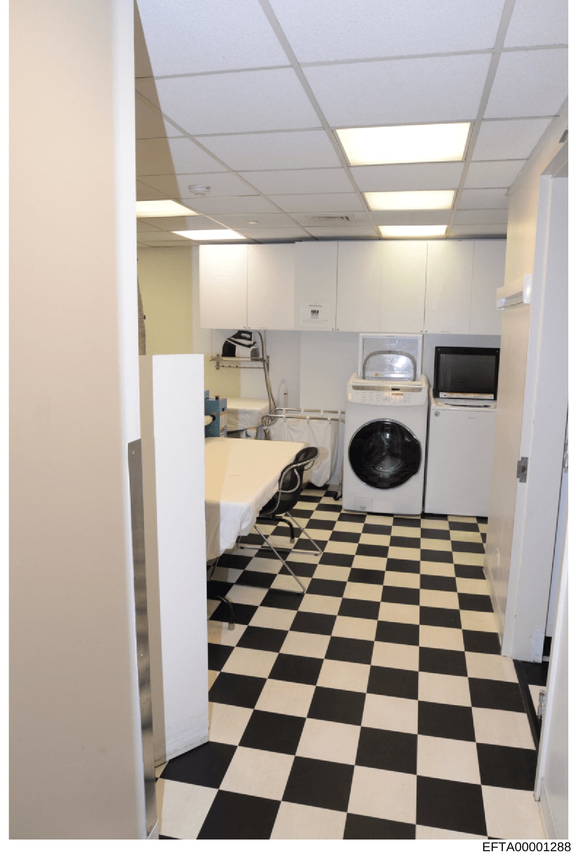 This is an evidence photograph showing the interior of a laundry room, likely from one of Epstein's properties. The image captures a utility space equipped with a washing machine, dryer, desk/work surface, and various appliances, with distinctive bla