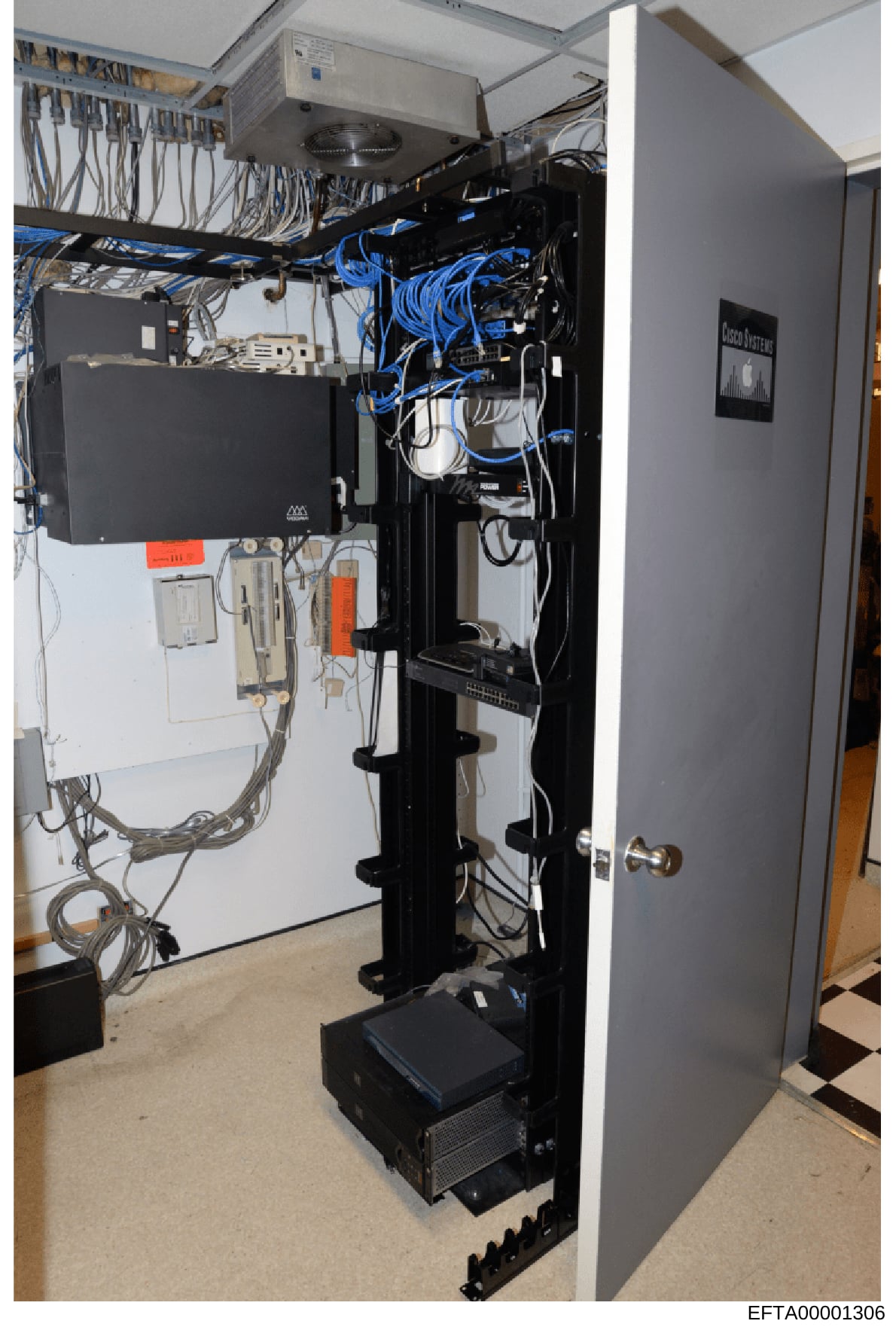 This photograph documents a server room or network closet containing various computer and networking equipment, including servers, switches, cables, and power distribution systems. The image shows a well-organized but densely wired infrastructure set