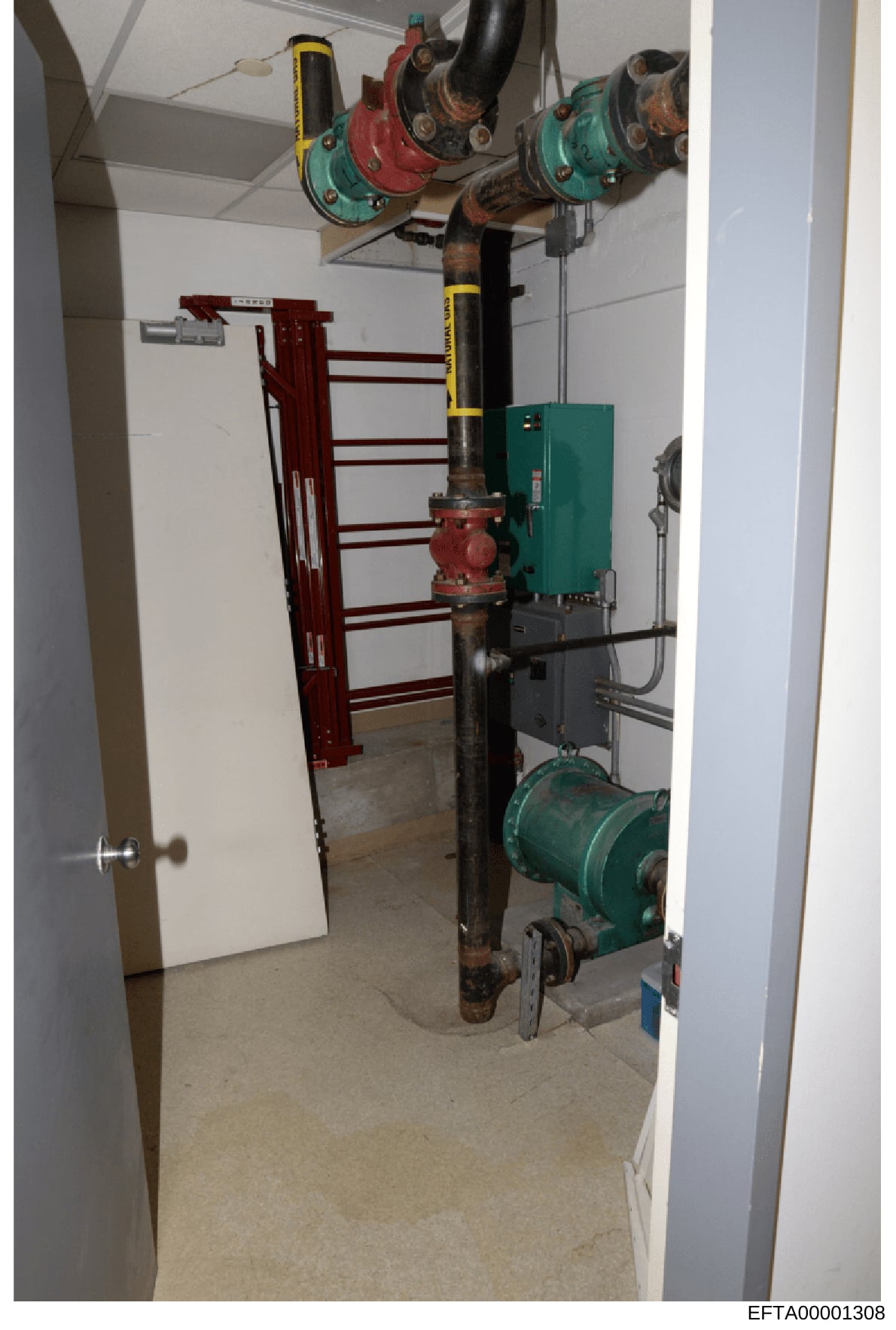 This is a photograph of a basement or utility room showing mechanical and HVAC equipment including pulleys, pipes, pumps, and a heating/cooling unit. The image documents the building's infrastructure and may be part of property inventory or structura