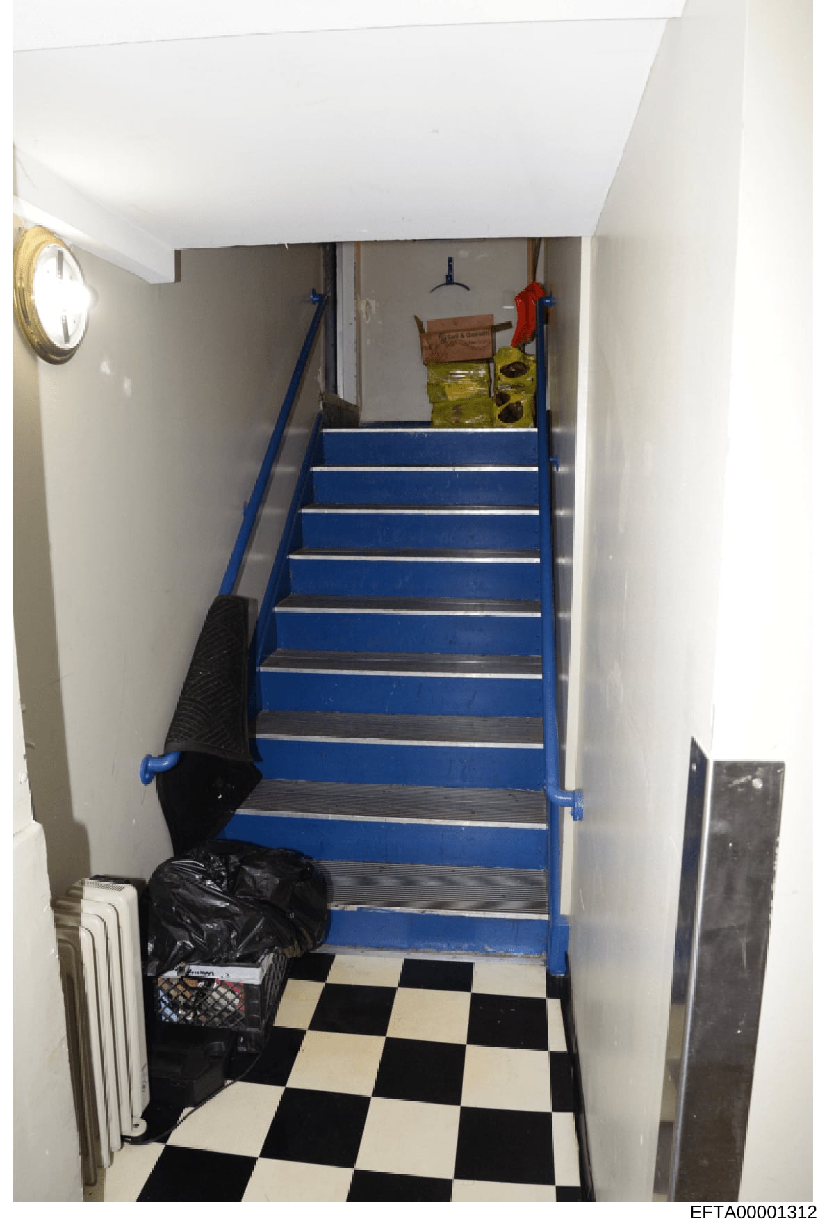 This is a photograph of an interior stairwell, likely from a residential or commercial property under investigation. The image shows a flight of blue and metallic steps leading upward, with white walls, a checkered black and white floor, and various 