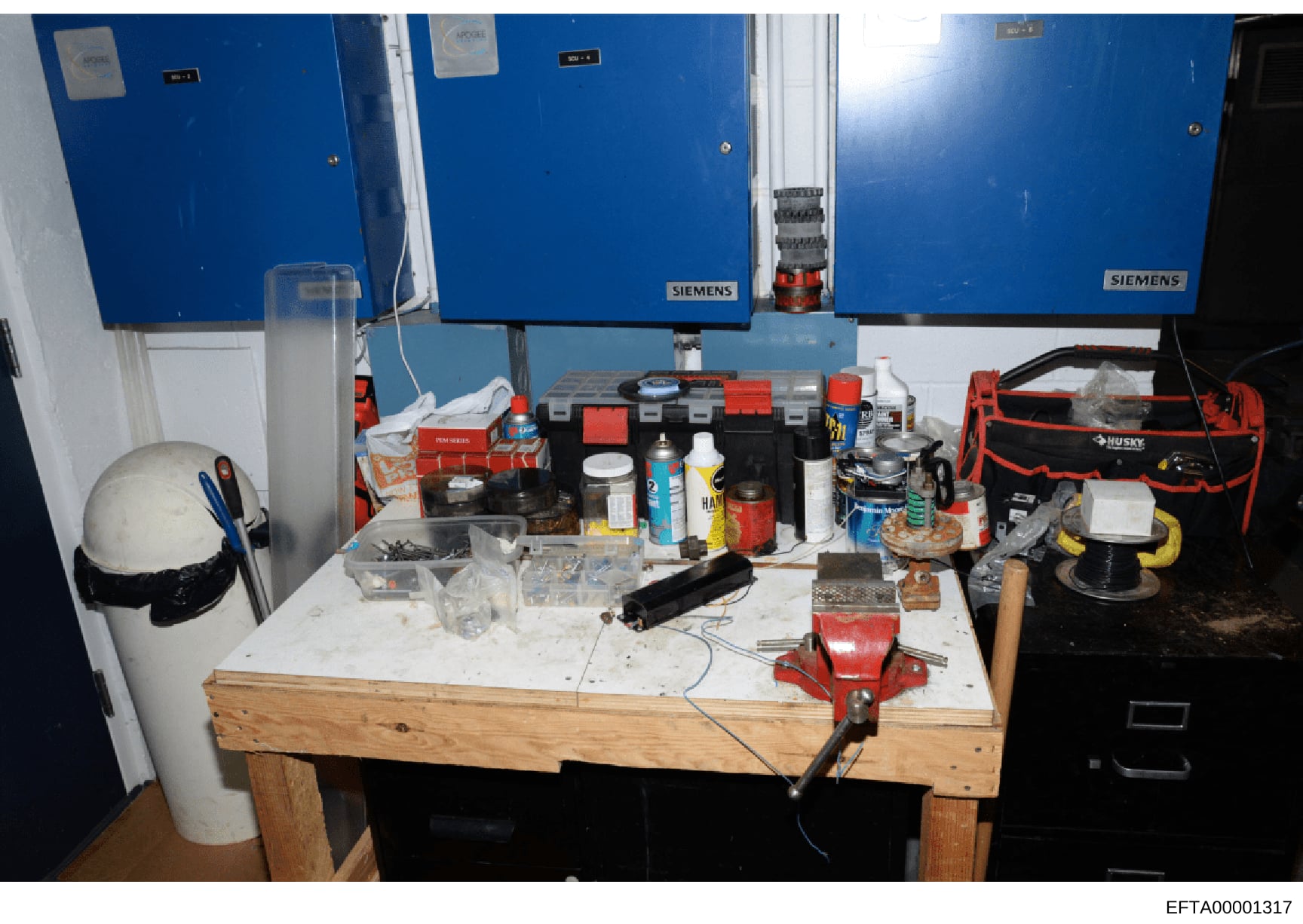 This is a photograph of a workshop or garage space showing a wooden workbench with various hand tools, power tools, hardware, and supplies. The image depicts blue electrical panels (Siemens brand) mounted on the wall, tool storage including a red Hus