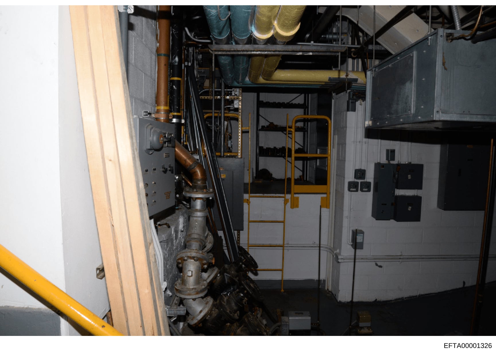 This is a photograph of an industrial or building systems room, showing mechanical and electrical infrastructure including HVAC piping, ductwork, electrical panels, and control systems. The image appears to be evidence documentation, possibly from a