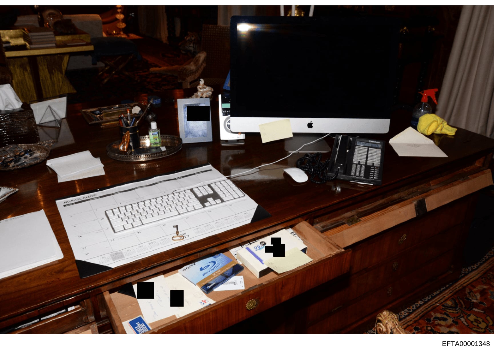 This is a photograph of an upscale office desk setup, likely from one of Jeffrey Epstein's properties based on the investigation file context. The image shows a wooden desk with multiple computers, keyboards, office supplies, and documents in drawers