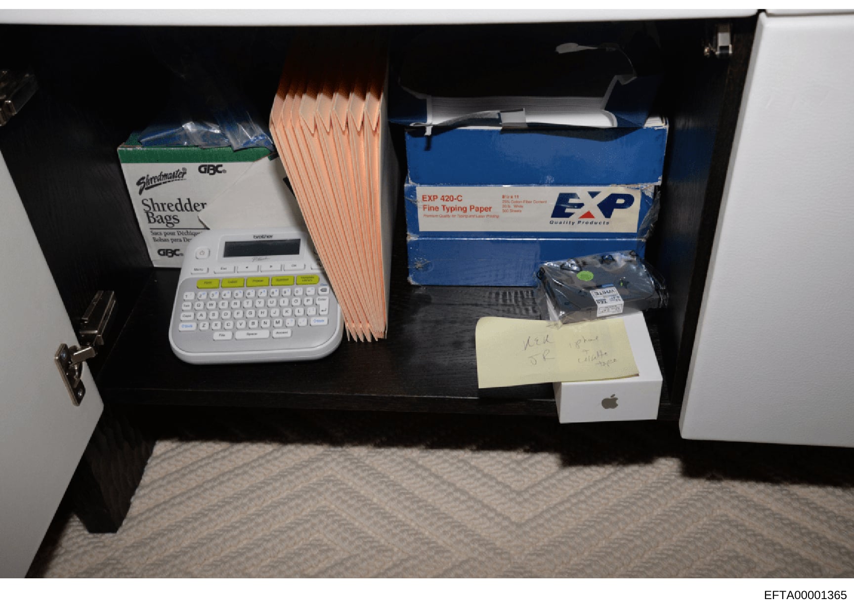 This photograph documents the contents of a desk drawer or office space, showing various items including office supplies, electronics, and paperwork. The image appears to be evidence documentation from the investigation, captured with a clear view of
