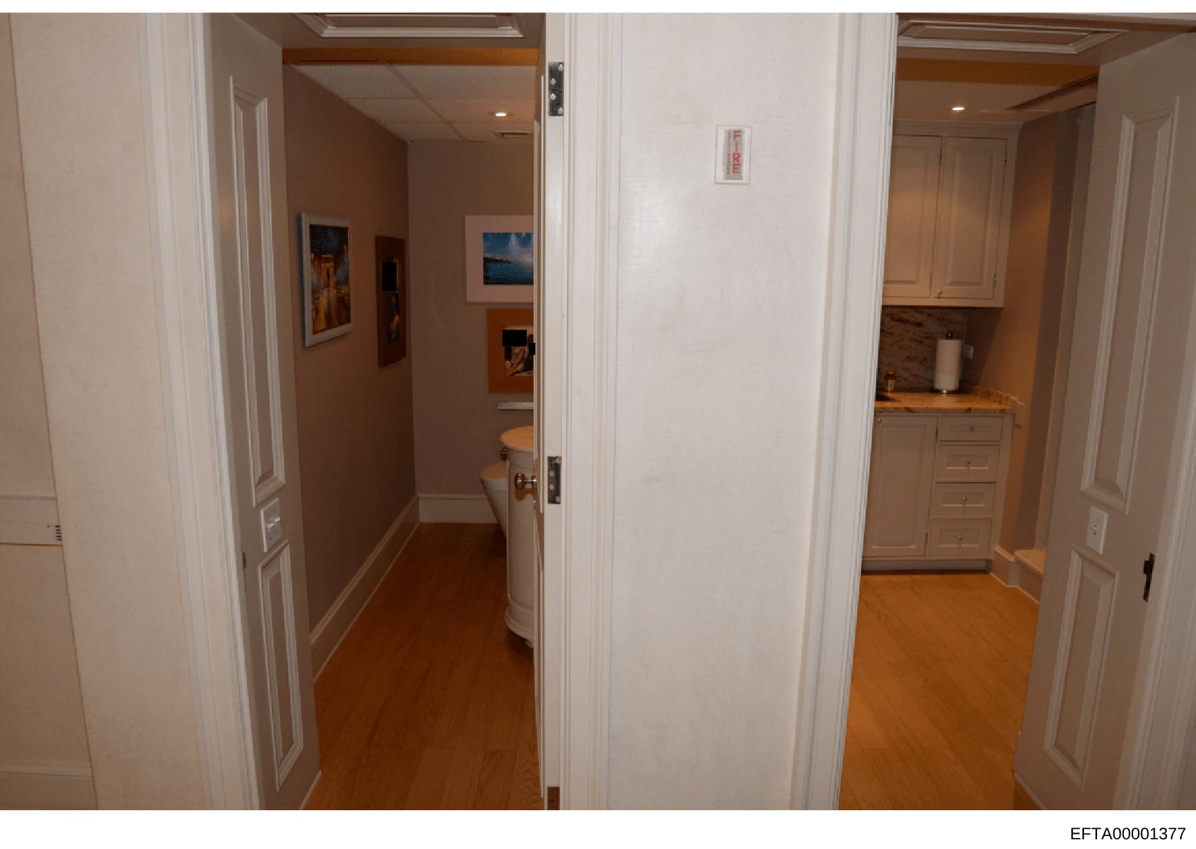 This is a photograph showing interior hallways and adjoining rooms of a residential property, including views of a bathroom with toilet visible, a kitchenette area with cabinets and countertop, and multiple doorways with white frames. The image appea