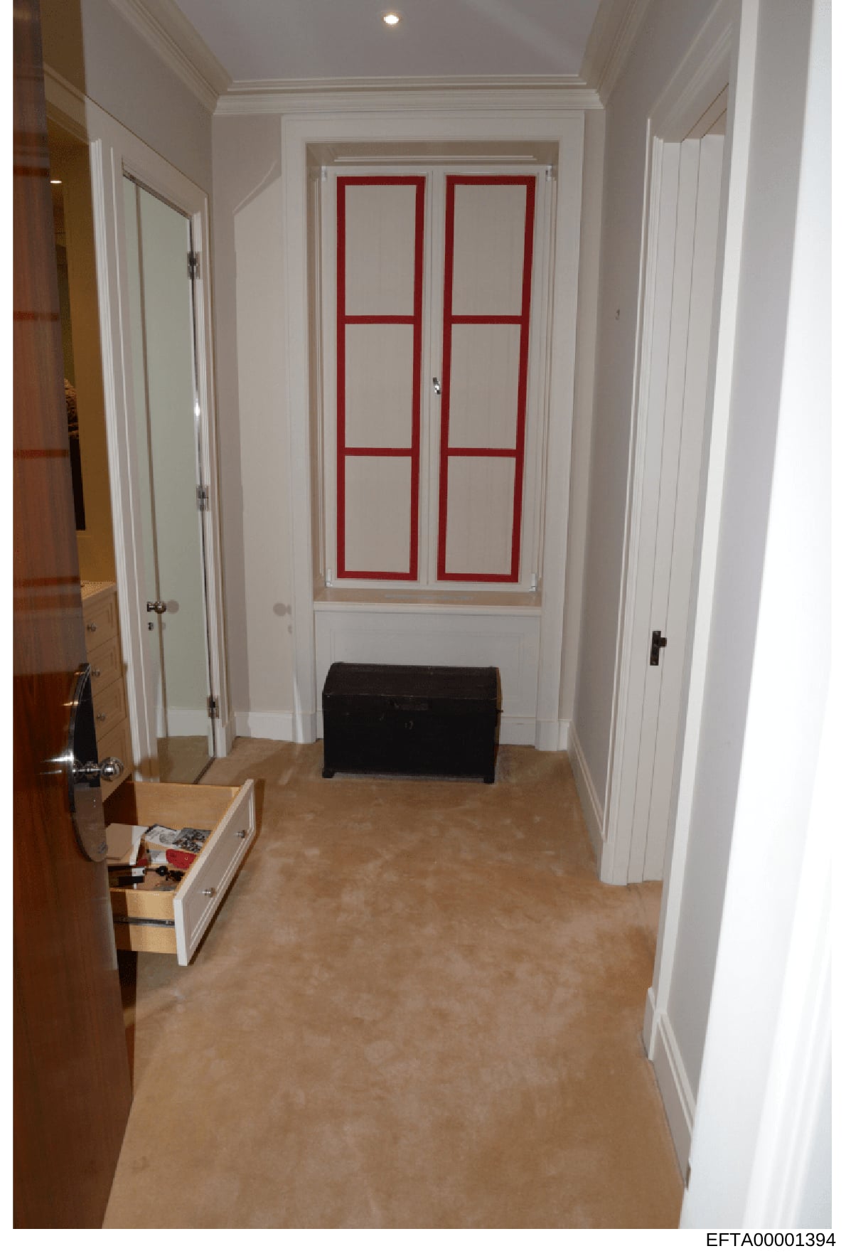 This photograph depicts an interior hallway of what appears to be a residential property, showing white painted walls, cream-colored flooring, multiple white doors on either side, and a distinctive pair of French doors with red frames in the center b
