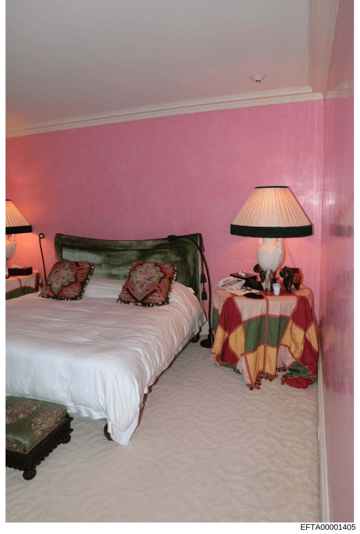 This is a photograph of an interior bedroom space, likely from one of Jeffrey Epstein's properties. The room features distinctive pink-painted walls, a bed with green headboard and decorative pillows, bedside lamps, and coordinated furnishings. The p