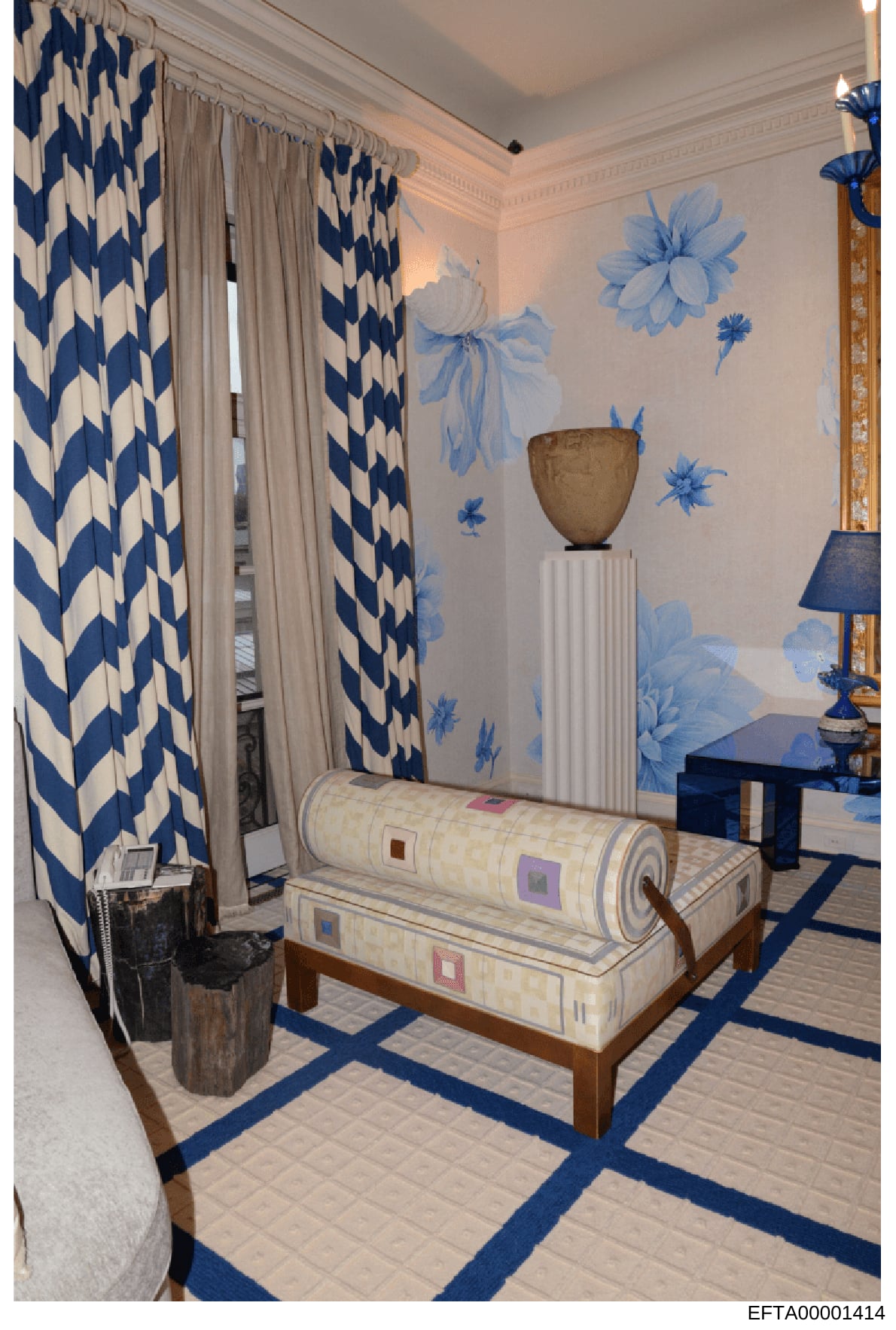 This is a photograph of an elegantly decorated interior room, likely a bedroom or dressing room, featuring blue and white color scheme decor. The room displays high-end furnishings including patterned curtains, wall murals, a pedestal with decorative