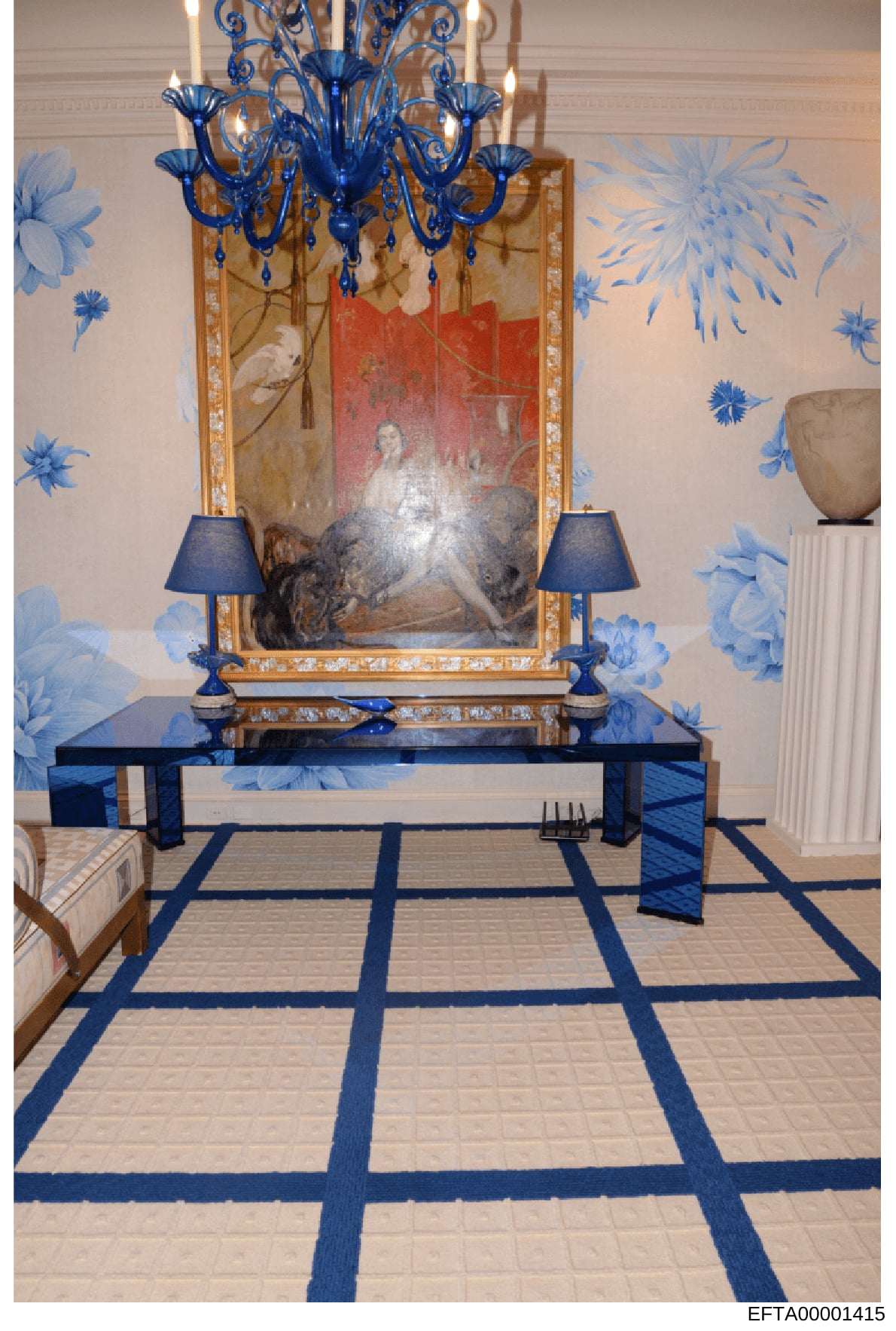 This is a photograph of an elegantly decorated interior room, featuring a sophisticated display with a blue Murano glass chandelier, ornate gold-framed mirror, portrait painting, and symmetrical blue table lamps. The room showcases high-end furnishin