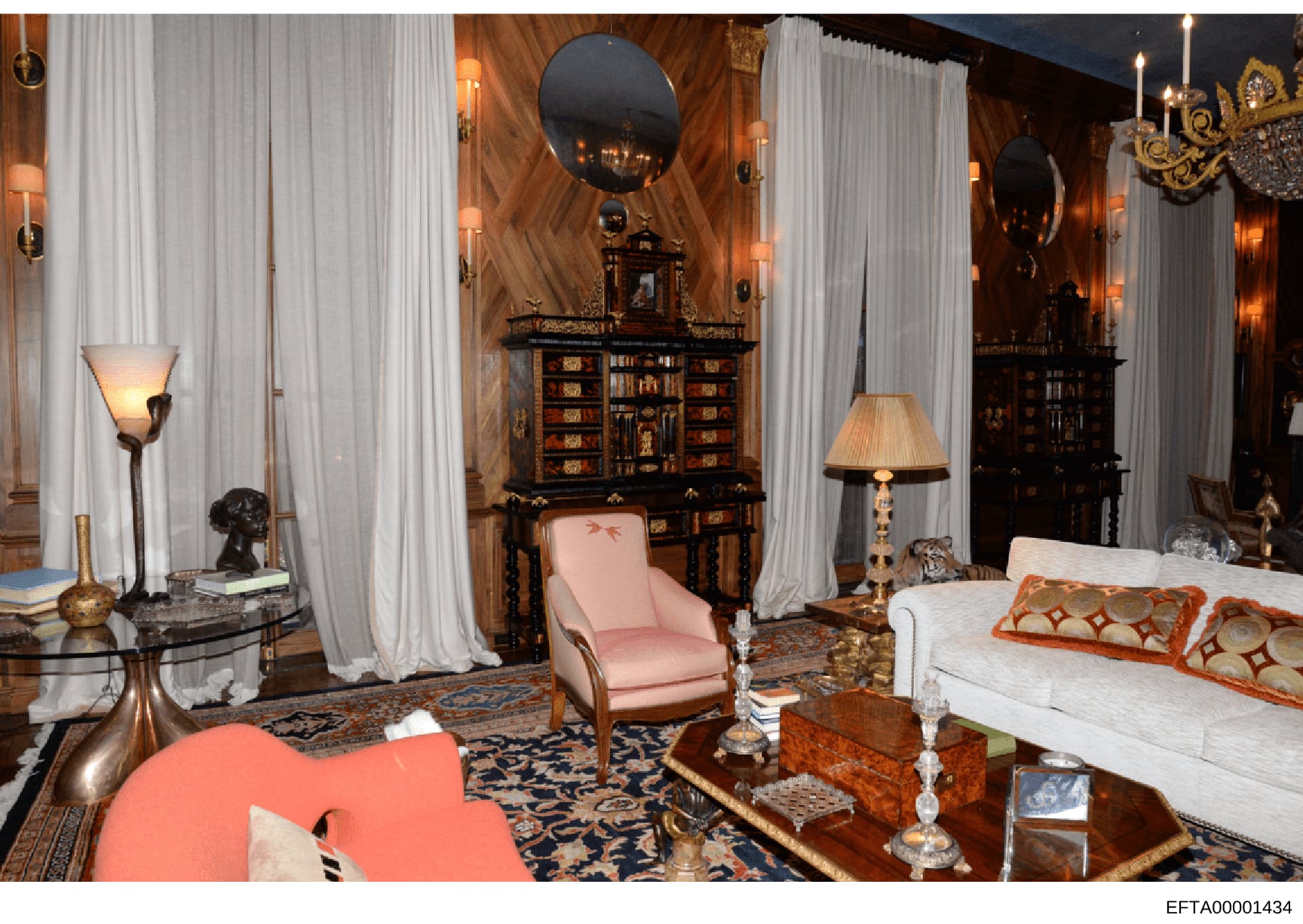 This photograph shows an elegantly decorated interior room featuring high-end furniture, including a pink upholstered chair, white sofa with decorative pillows, dark wood cabinetry with inlaid details, multiple mirrors, brass and crystal lighting fix