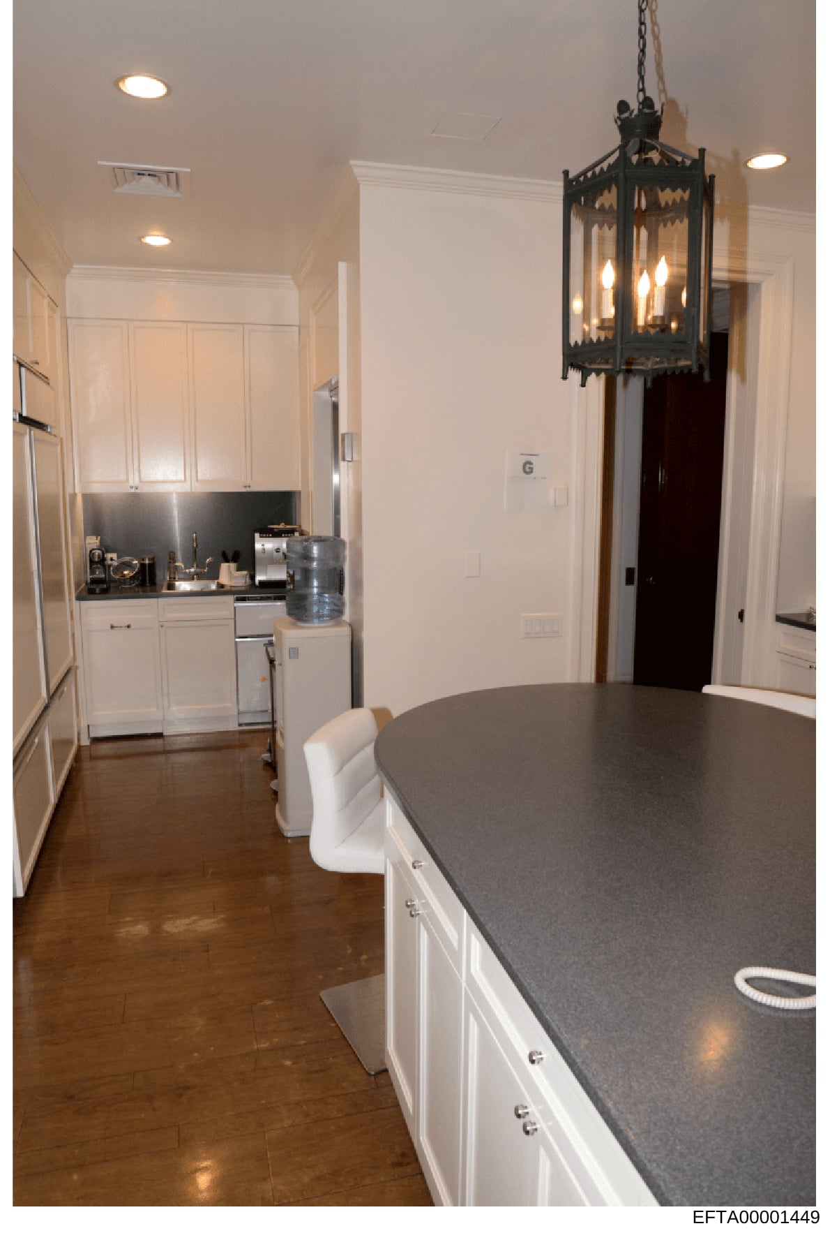 This is a photograph of a luxury kitchen and dining space showing high-end finishes and décor. The image depicts a modern kitchen with white cabinetry, black countertops, stainless steel appliances, recessed lighting, and a decorative black pendant f
