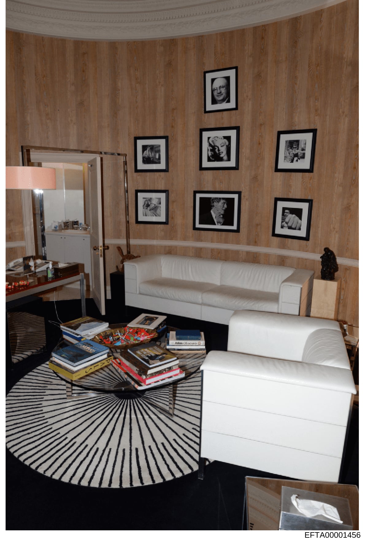 This is an evidence photograph depicting the interior of a residential room, likely from one of Jeffrey Epstein's properties. The room features wood-paneled walls with multiple framed black-and-white photographs, contemporary furniture including whit