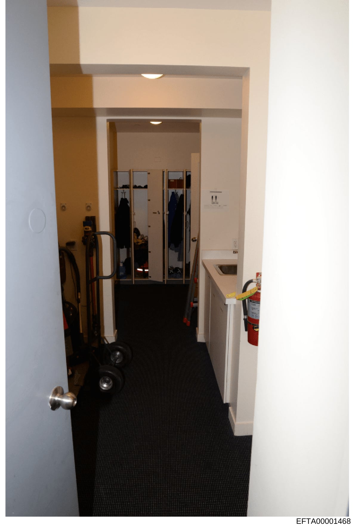 This is a photograph of an interior hallway or corridor, showing built-in mirrored wardrobe doors, utility equipment including a hand truck and fire extinguisher, and basic facility furnishings. The image appears to be evidence documentation from a p