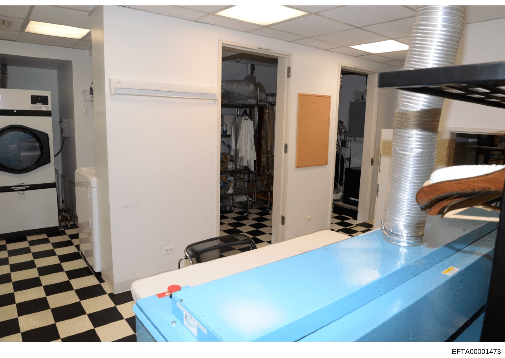 This is an evidence photograph showing the interior of a laundry and utility room, featuring commercial-grade washing and drying equipment, storage areas, and a black-and-white checkered floor. The photo documents the layout and condition of domestic