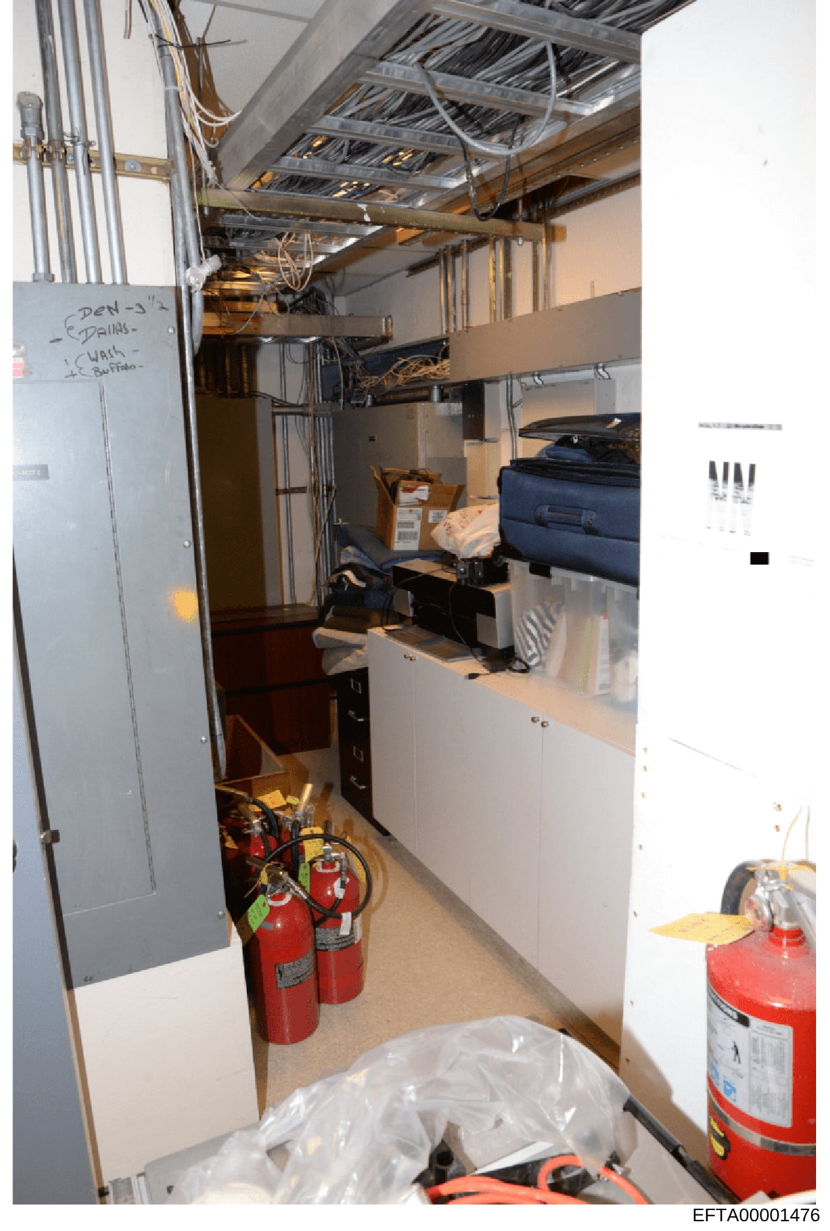 This photograph shows a basement utility room or mechanical space containing HVAC equipment, electrical infrastructure, fire extinguishers, and miscellaneous storage items. The space includes exposed ductwork, piping, electrical conduit, and handwrit