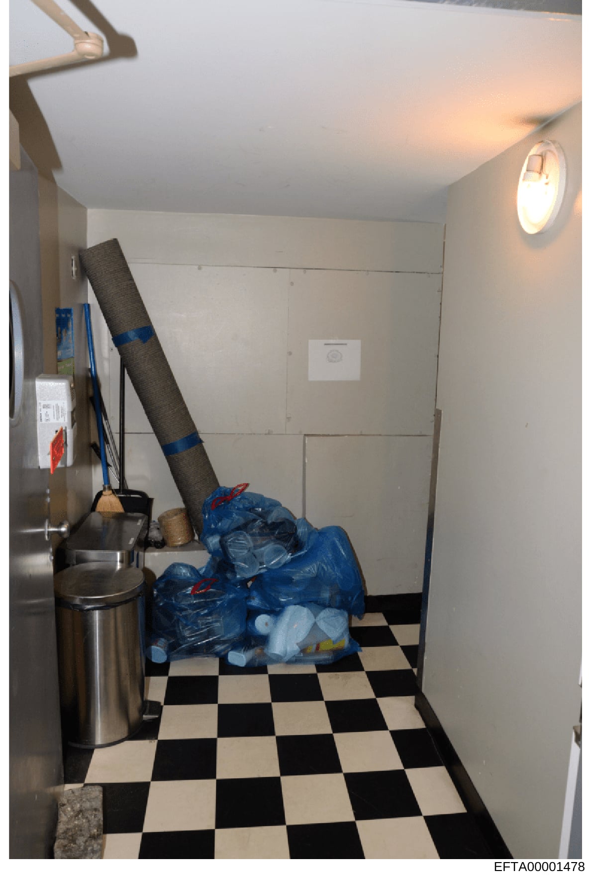 This photograph shows the interior of a utility or storage room, likely from one of Jeffrey Epstein's properties. The image depicts a small room with a black and white checkered tile floor, white walls, recessed lighting, and various items including