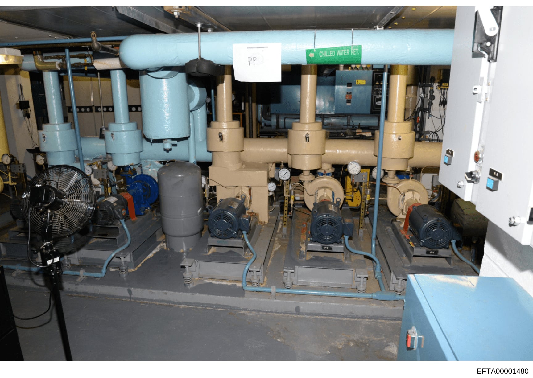 This photograph shows the interior of a mechanical/utility room containing industrial pumping equipment, including multiple centrifugal pumps, a chilled water retention system (marked with green label), piping infrastructure, and auxiliary equipment.