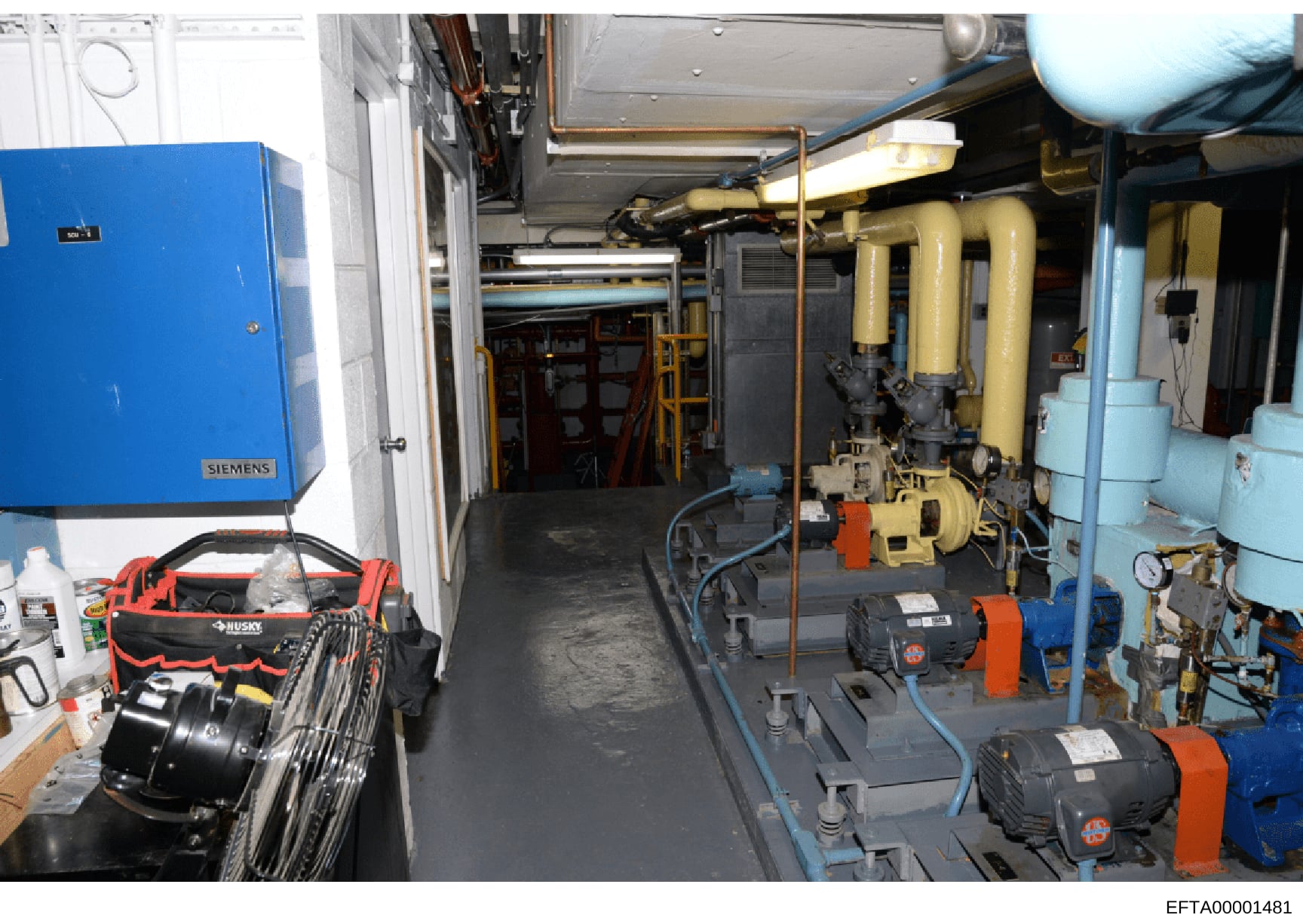 This photograph shows an industrial or commercial mechanical room containing HVAC equipment, pumps, pipes, electrical systems, and various tools. The image documents building infrastructure including a Siemens blue electrical panel, yellow piping sys