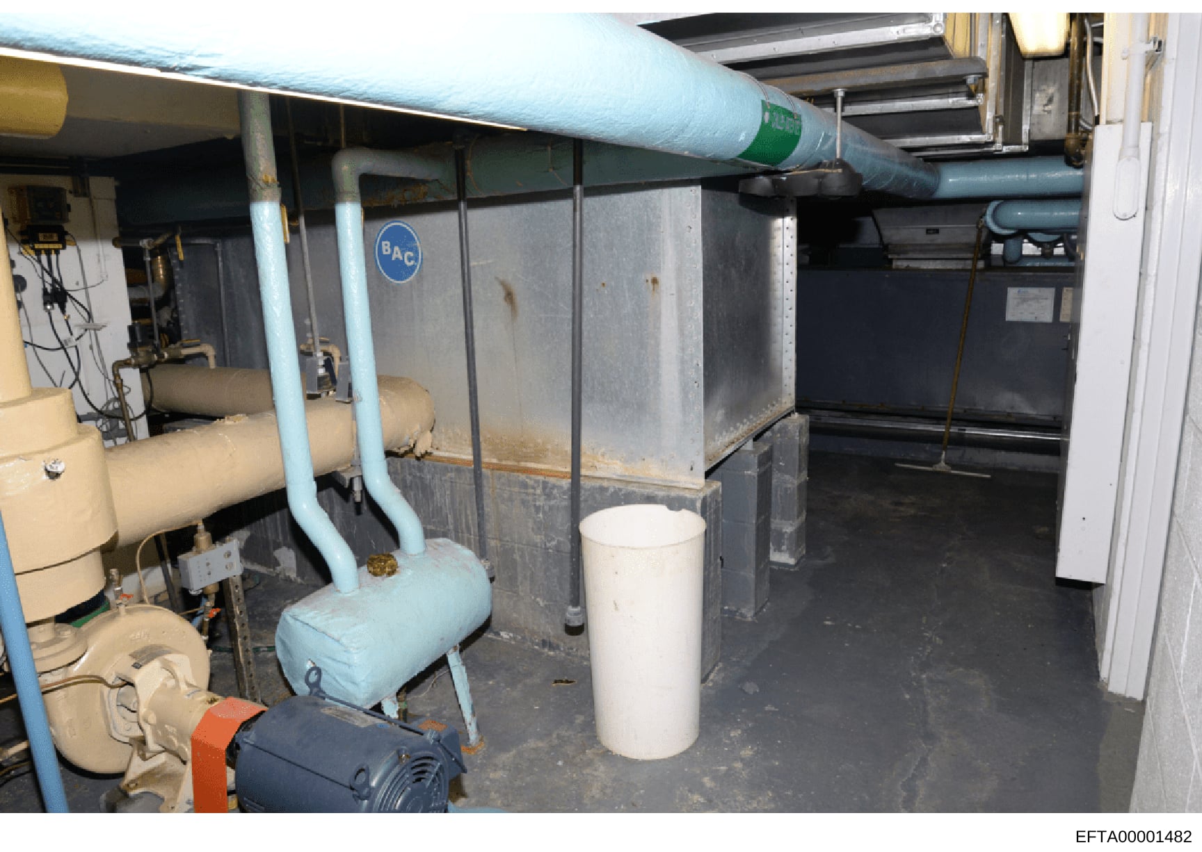 This is a photograph of a basement mechanical/utility room, likely from one of Epstein's properties. The image shows various HVAC equipment, pipes, tanks, and infrastructure systems. The photograph appears to be evidence documentation from the invest