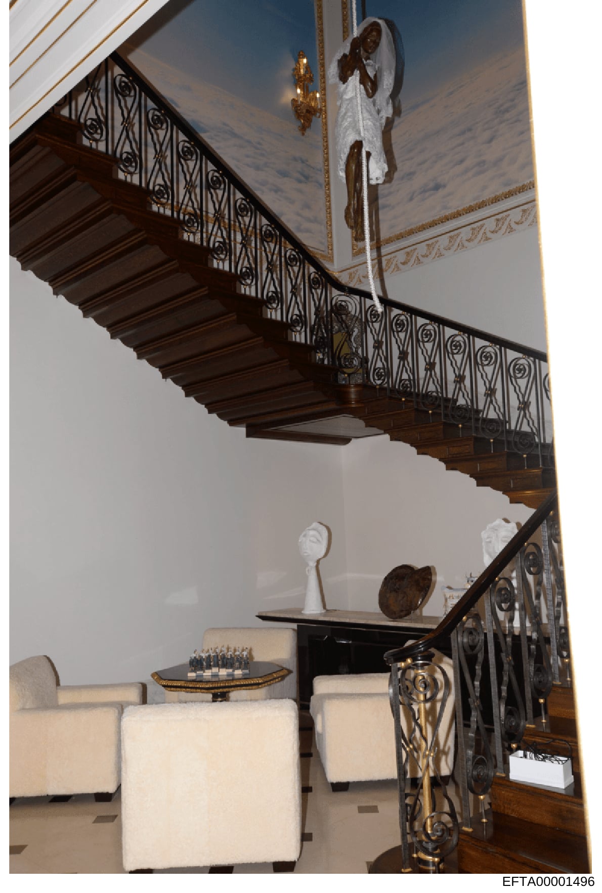 This is a photograph of an ornate interior space featuring a sweeping wooden staircase with decorative iron railings, classical ceiling details, and luxury furnishings. The image shows the architectural design and décor of what appears to be a high-e