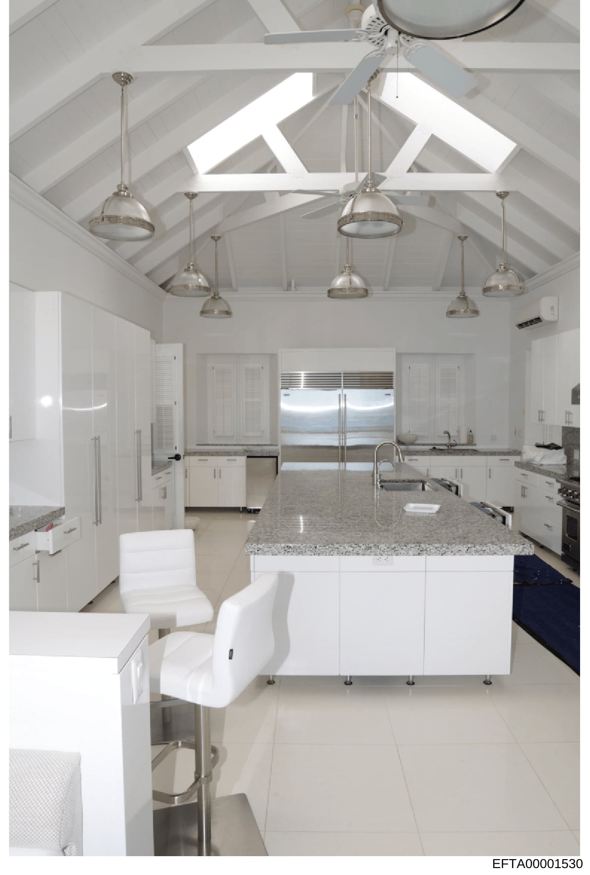 This is a photograph of a contemporary kitchen space featuring white cabinetry, granite countertops, stainless steel appliances, and an open floor plan with vaulted ceilings and skylights. The image appears to be documentation of interior design or p