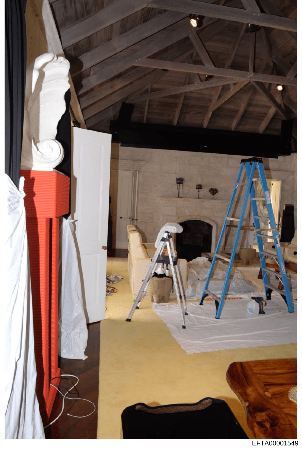 This photograph shows an interior space under active renovation or construction, featuring exposed wooden ceiling beams, ladders, protective coverings, and ongoing work. The room appears to be a large space with high ceilings and a fireplace, suggest