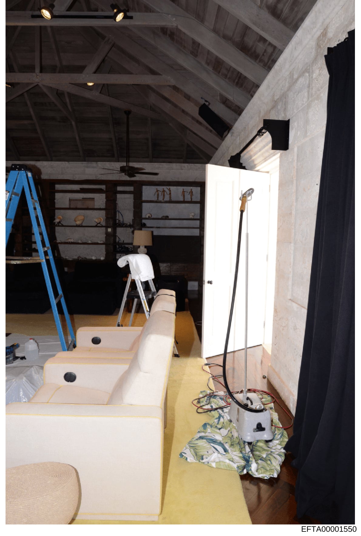 This photograph documents an interior space during renovation or construction, showing built-in seating with cream-colored cushions, exposed ceiling beams, shelving units, and various construction materials. The image appears to be from a property in