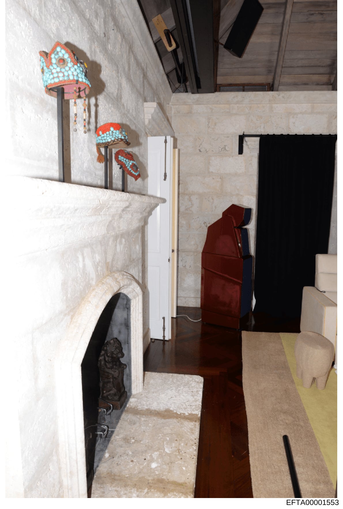 This is an evidence photograph showing an interior room space, likely from one of Jeffrey Epstein's properties. The image captures a fireplace with a dark ornamental insert, white marble or stone walls, decorative beaded objects mounted on the wall (