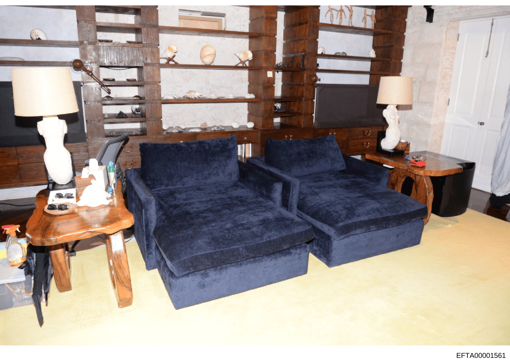 This photograph documents the interior of a high-end residence, showing a contemporary living room with custom built-in wooden shelving, two navy blue upholstered seating pieces, modern white sculptural lamps, and decorative accessories. The image ap